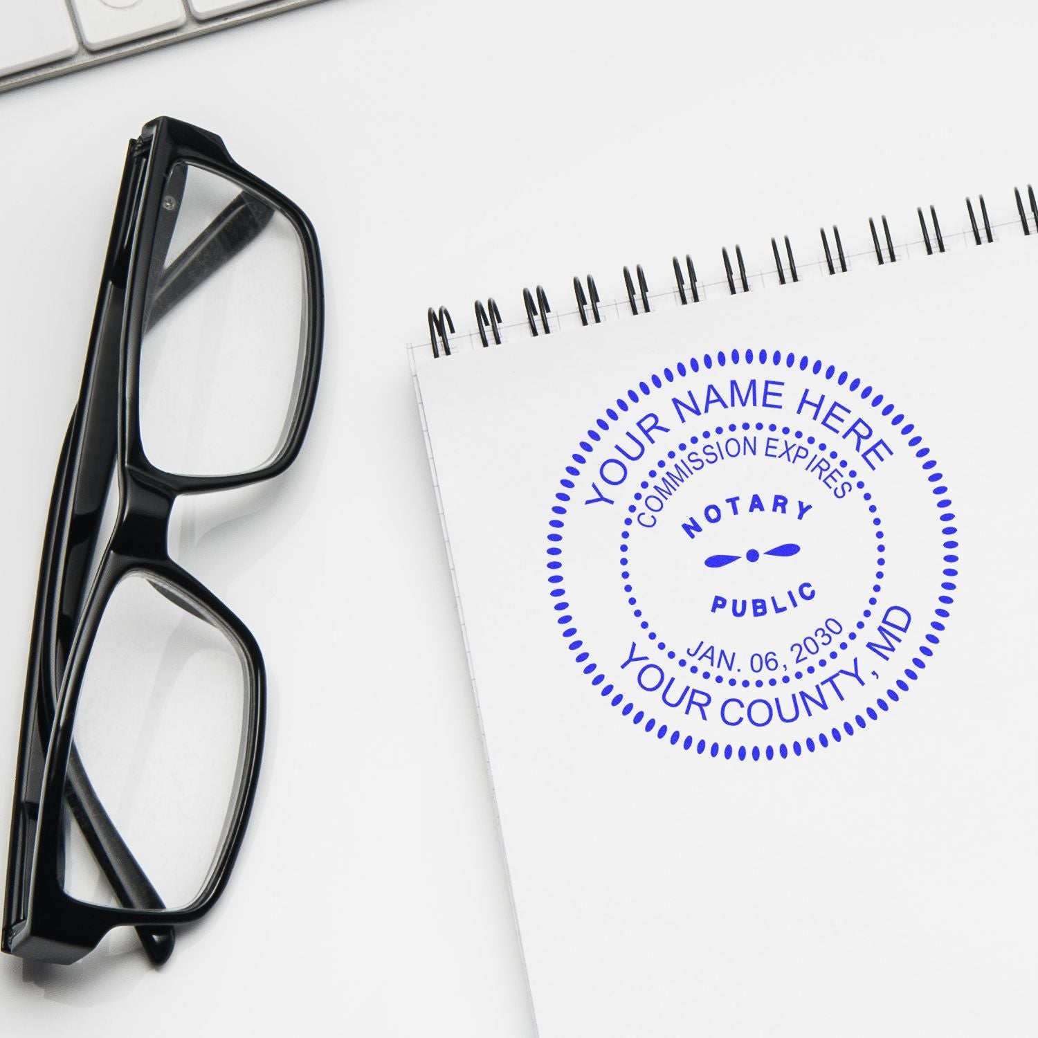 Black eyeglasses beside a notary public stamp notebook on a white desk with keyboard, legal office workspace concept.