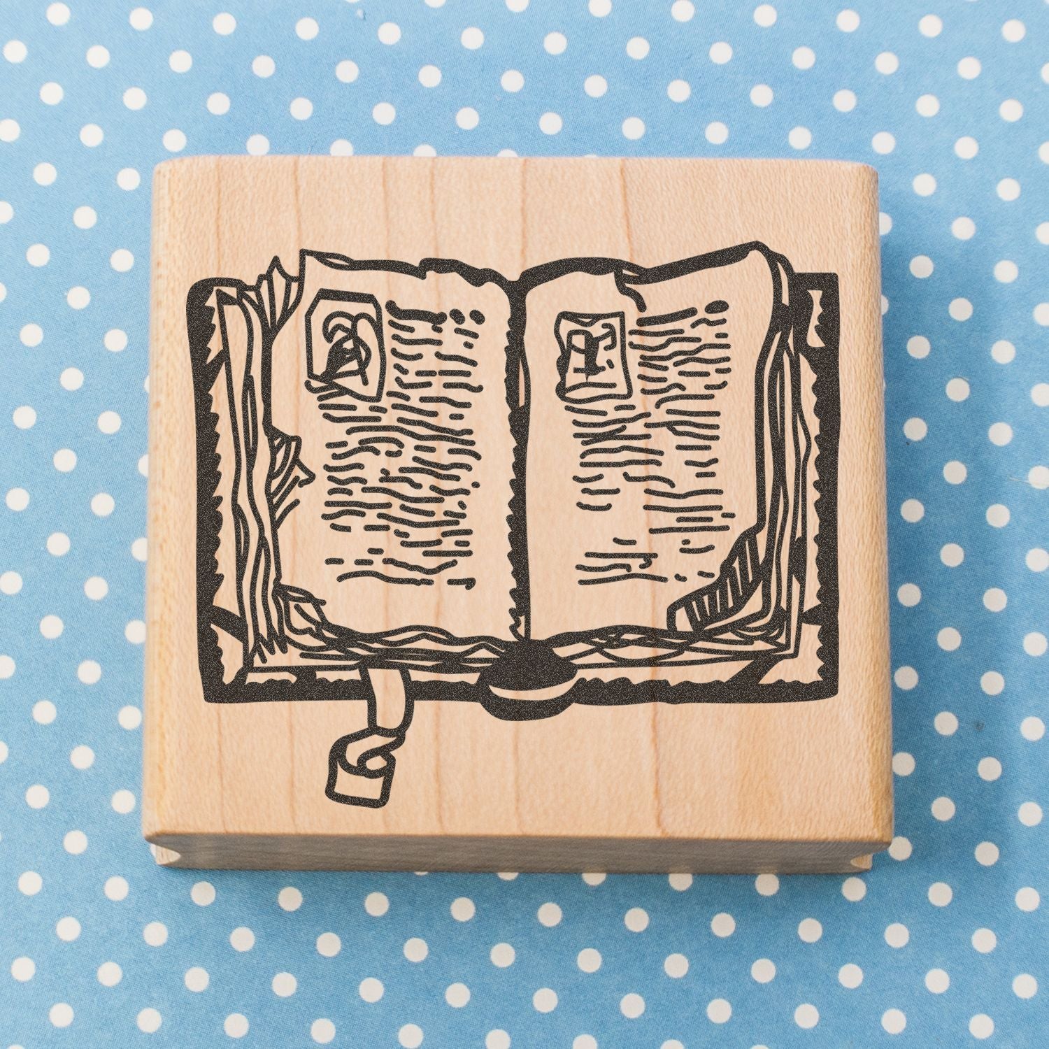 Wooden rubber stamp with open book illustration on blue polka dot fabric background