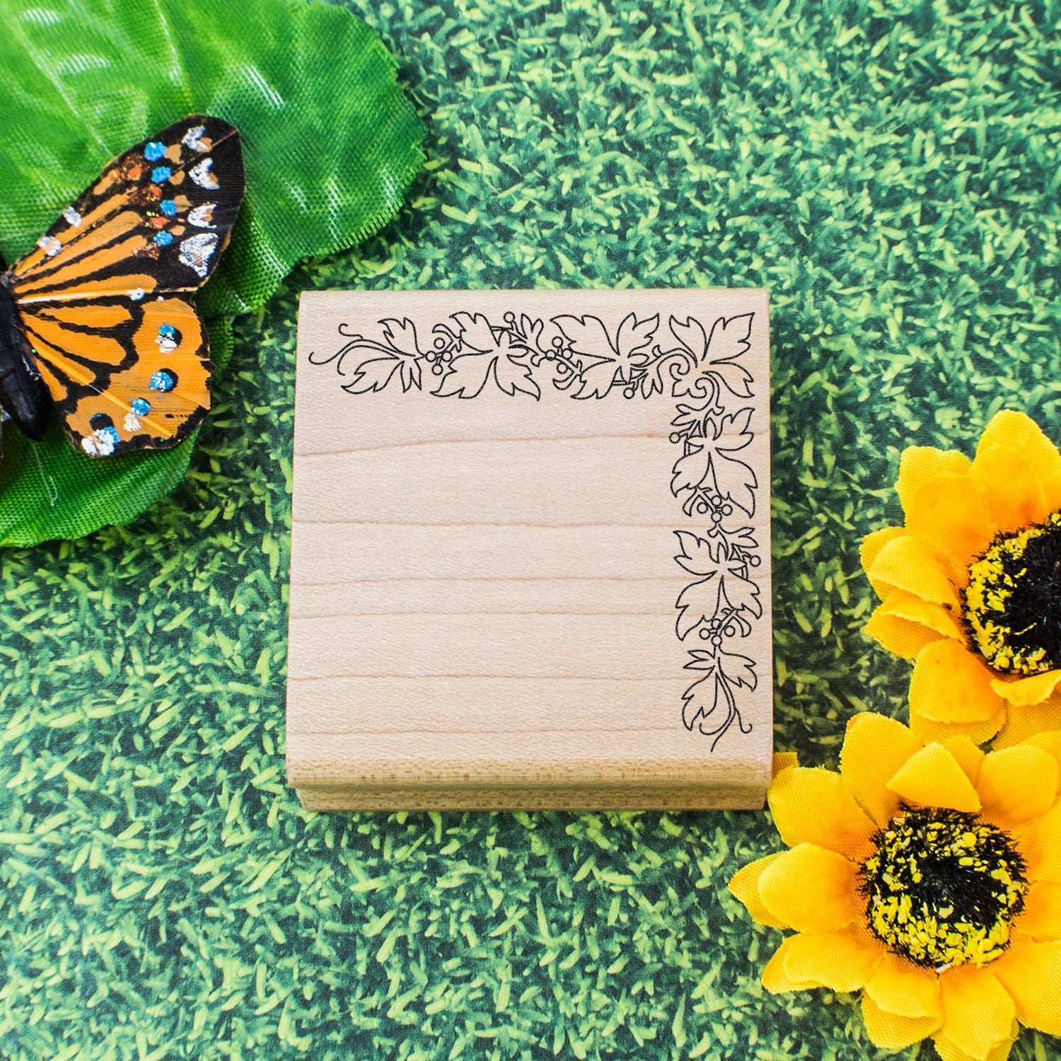 Wooden leaf border stamp with butterfly and sunflowers on green grass background for nature-themed crafts
