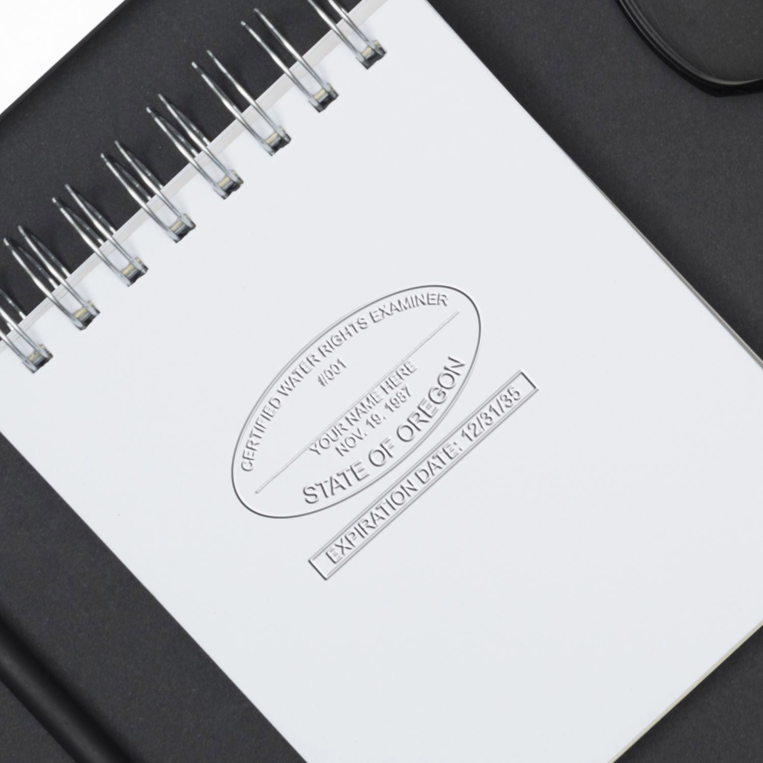 Close-up of spiral notebook with embossed State of Oregon certified water rights examiner stamp on a white page, business document concept.