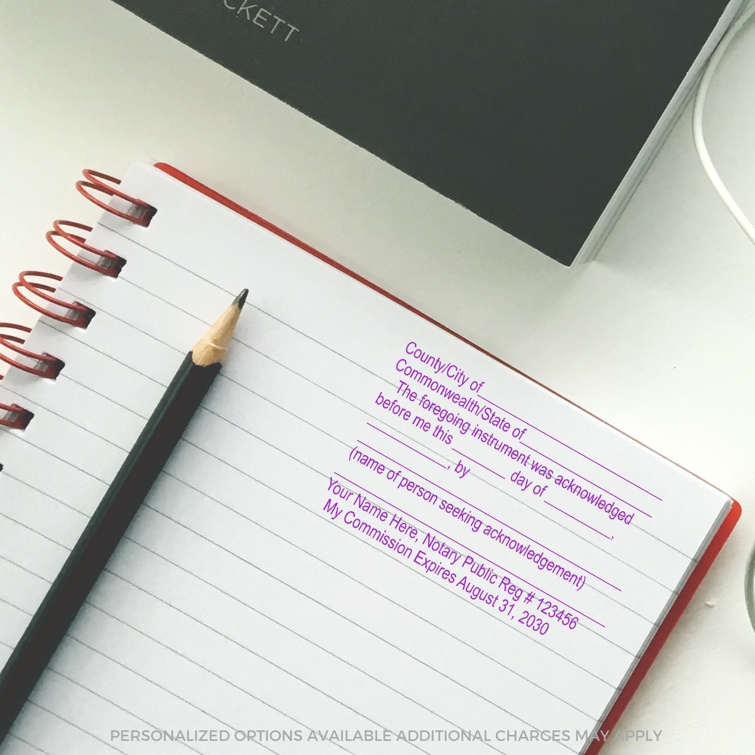 Spiral notary acknowledgment journal with pencil and personalized text template on a white desk.