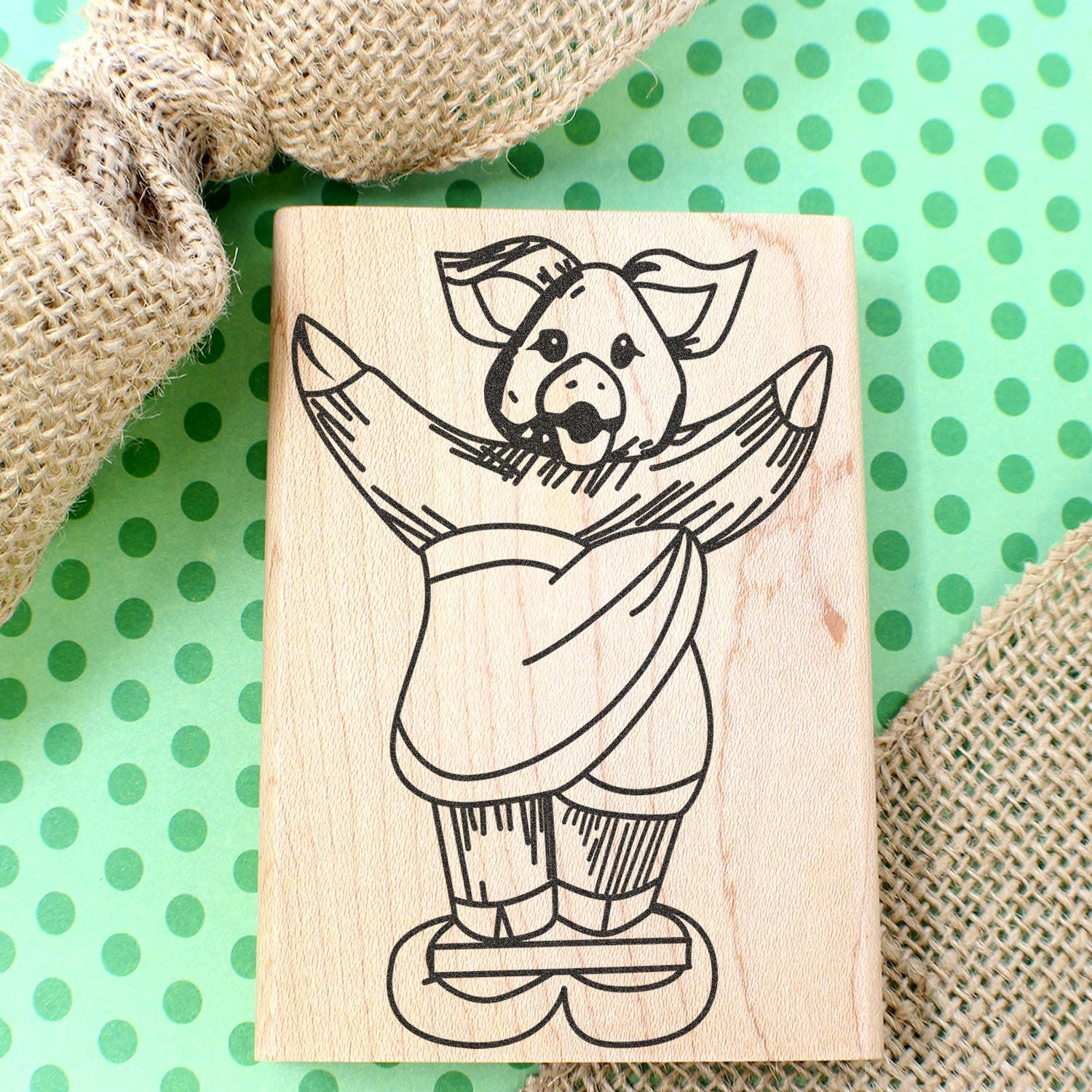 Wooden rubber stamp with cute pig illustration on a green polka dot background and burlap fabric.