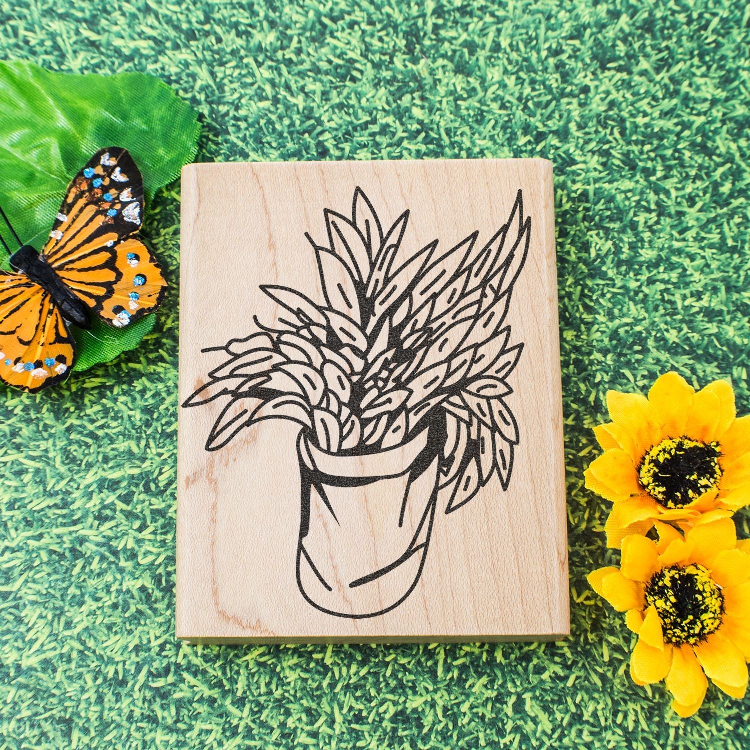 Botanical wooden decor with engraved potted plant, butterfly, and yellow flowers on grass background