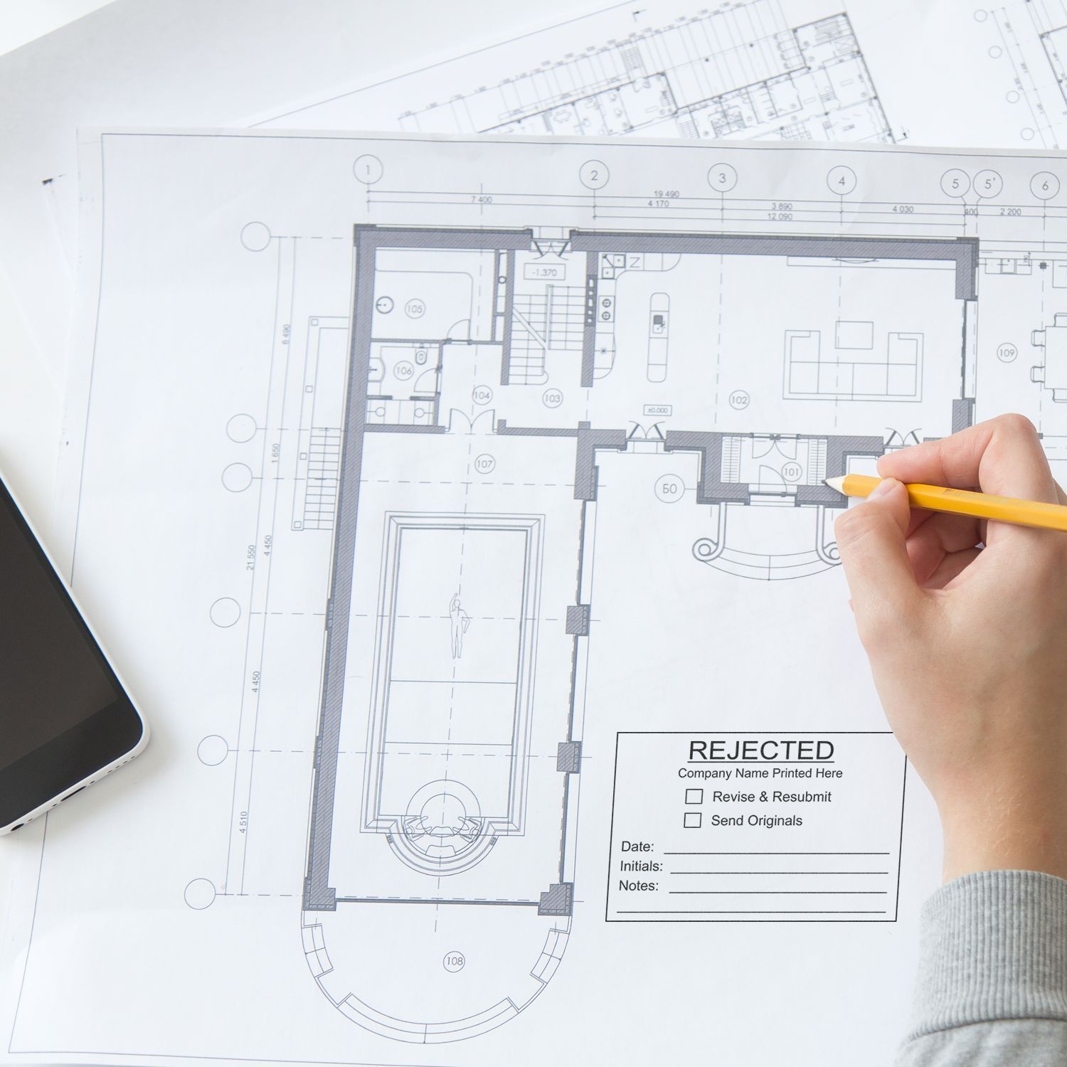 Hand marking an architectural floor plan blueprint with a yellow pencil and rejected stamp, concept of building design review and revision.