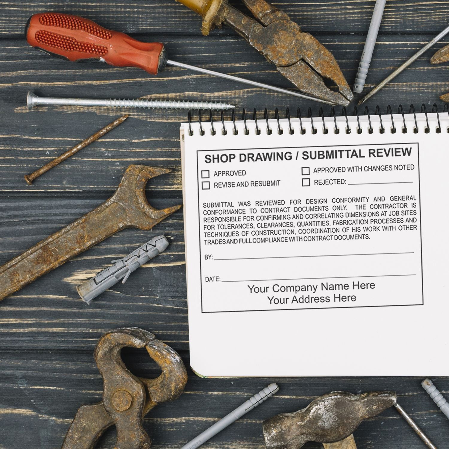 Construction tools and shop drawing submittal review form on a wooden desk, with rusty pliers, screwdriver, nails, and wall anchors.