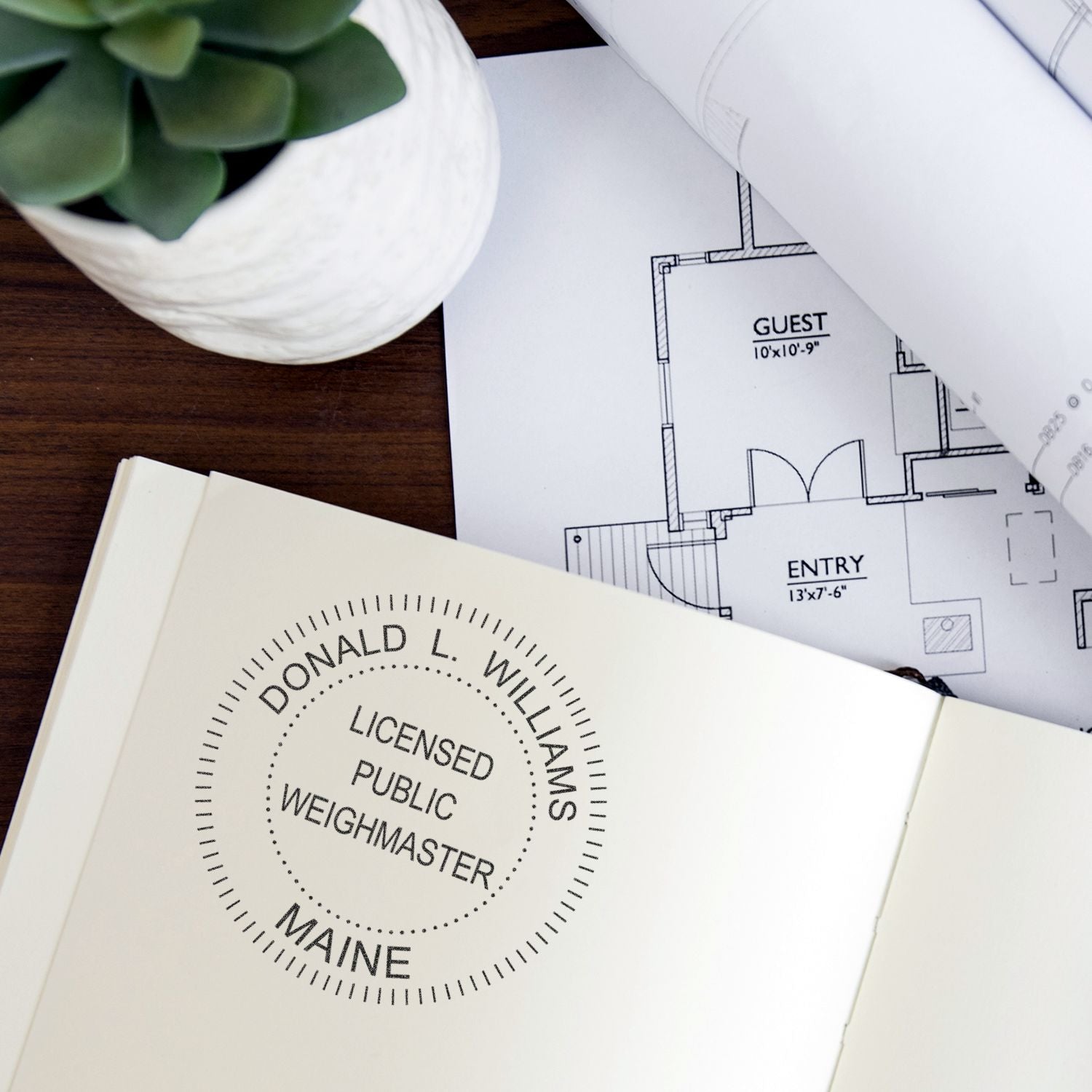 Architectural floor plans with notebook, potted succulent, and licensed public weighmaster stamp on desk.
