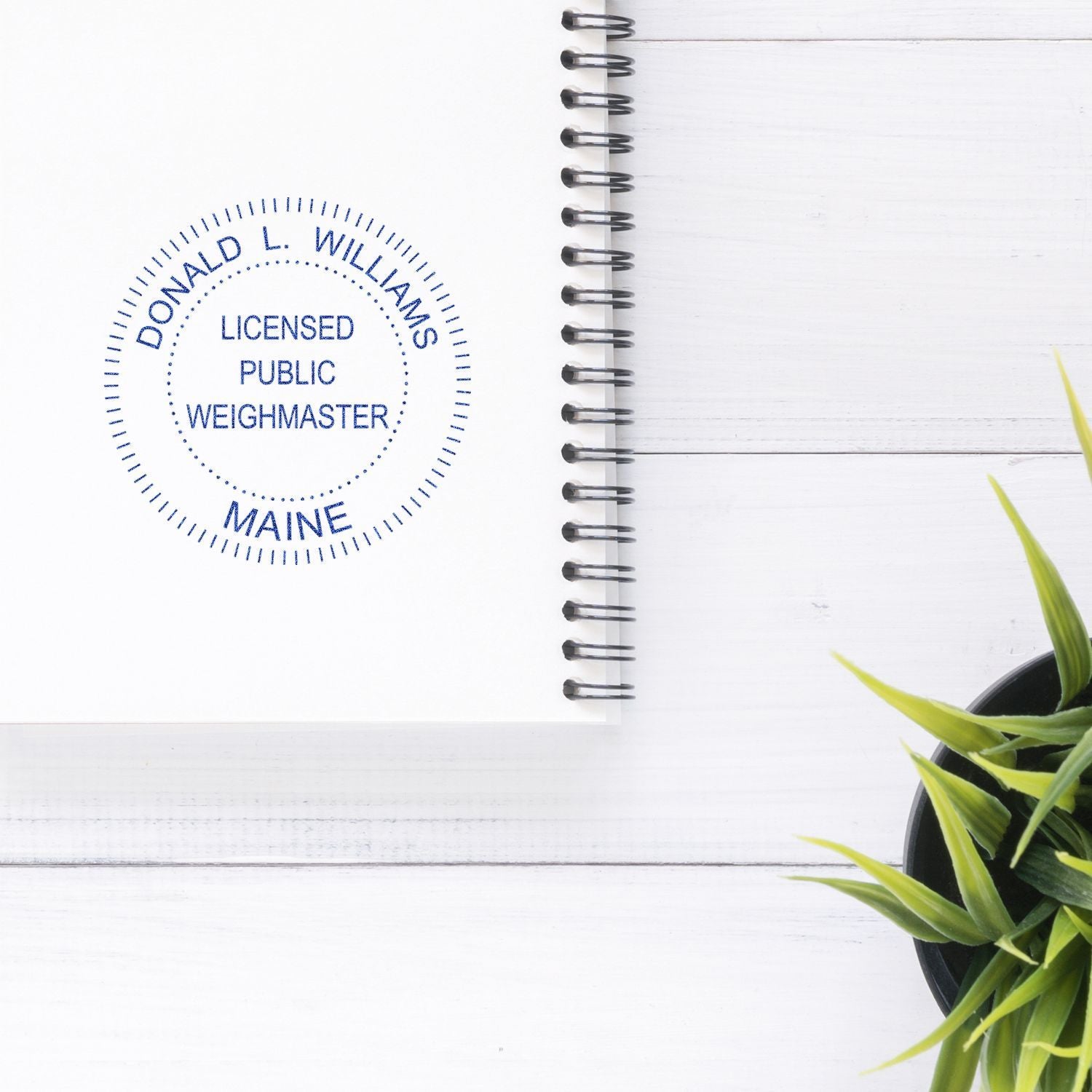 White spiral notebook with Donald L. Williams licensed public weighmaster Maine stamp on a wooden desk beside a small green potted plant.