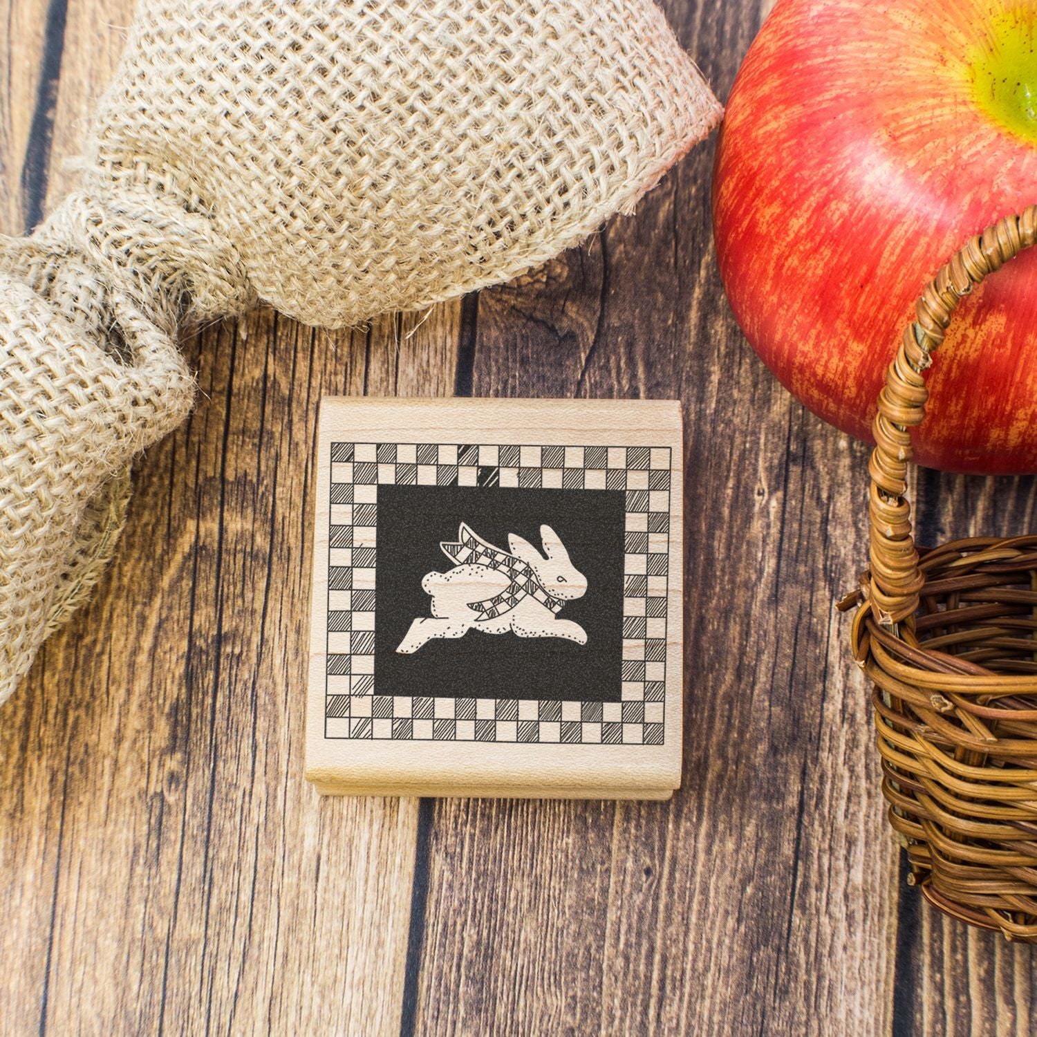 Rustic autumn still life with red apple, wicker basket, burlap sack, and wooden rabbit stamp on a wooden background