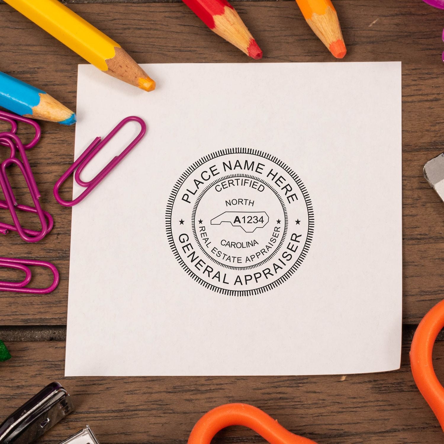 Blank paper with North Carolina general real estate appraiser stamp, surrounded by colored pencils and paper clips on a wooden desk.
