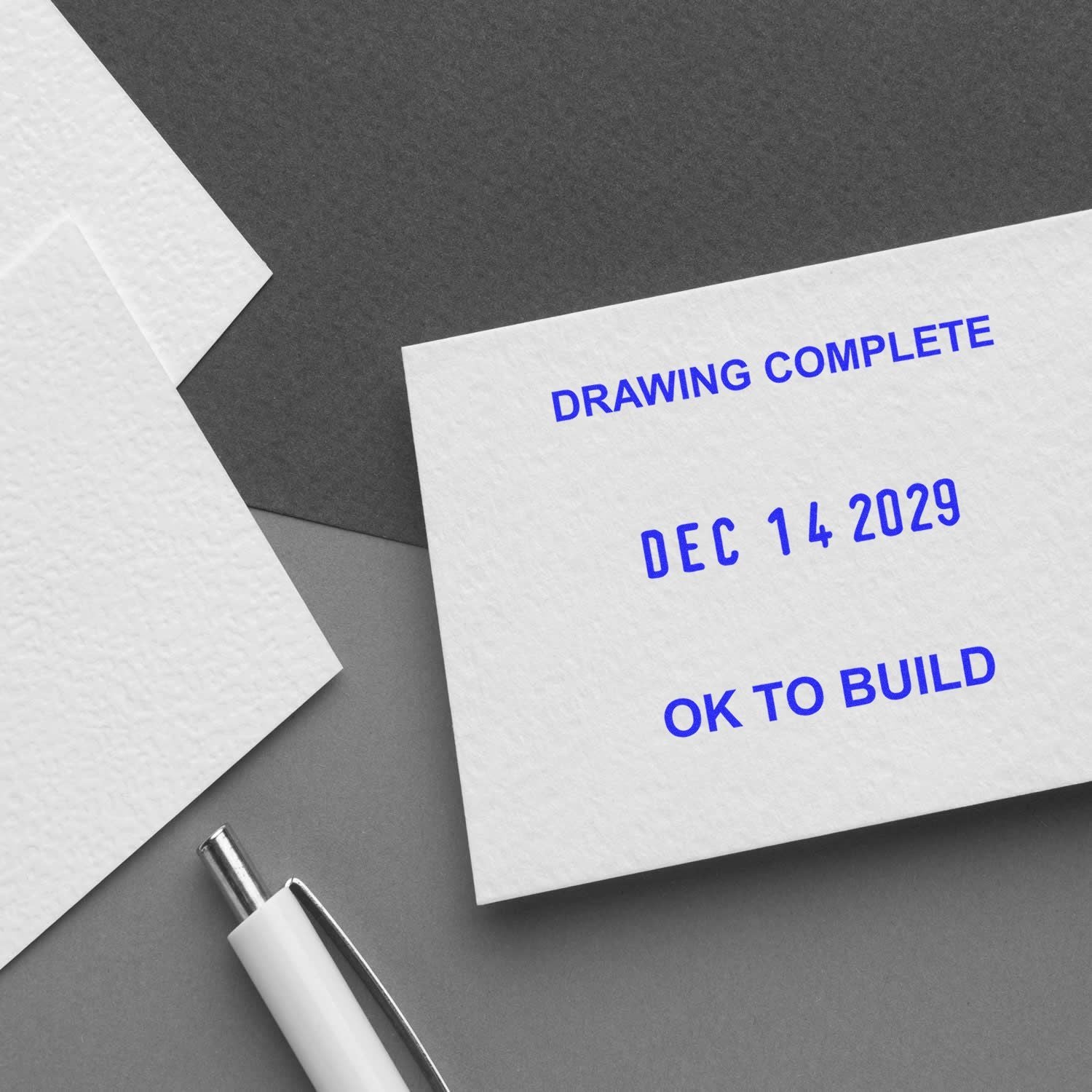 Stamped construction drawing complete document with OK TO BUILD approval date and pen on desk.