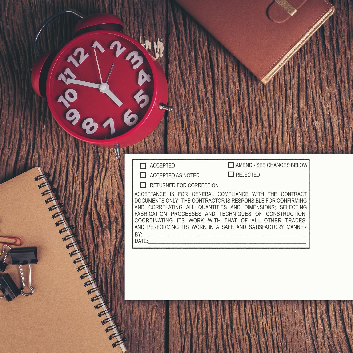 Red alarm clock beside notebook and contract approval form on a wooden office desk.