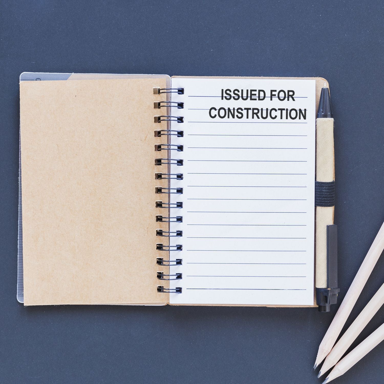 Open notebook with Issued for Construction title page, spiral binding, and pencil on dark background.