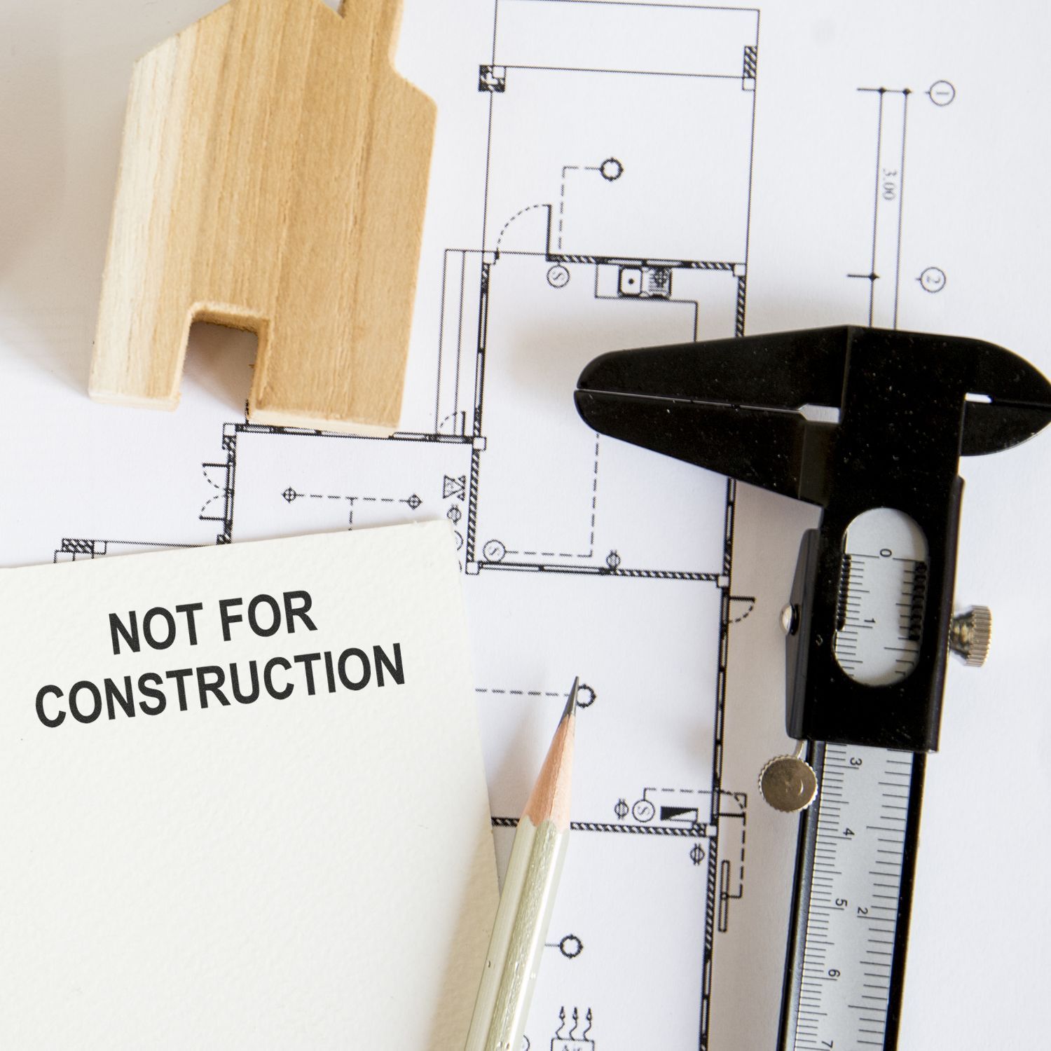Architectural blueprint with caliper, pencil, wood sample, and Not for Construction note for building design and measuring.
