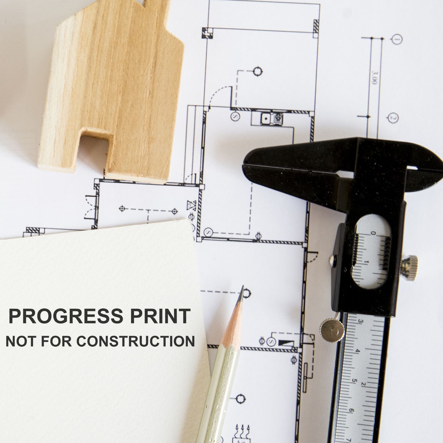 Architectural floor plan with measuring caliper, pencil, and wood sample on a progress print not for construction.