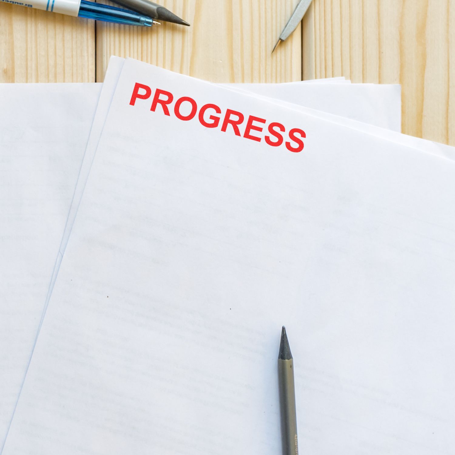 Blank report pages with PROGRESS in red on a wooden desk, with pens and office stationery, business growth concept.