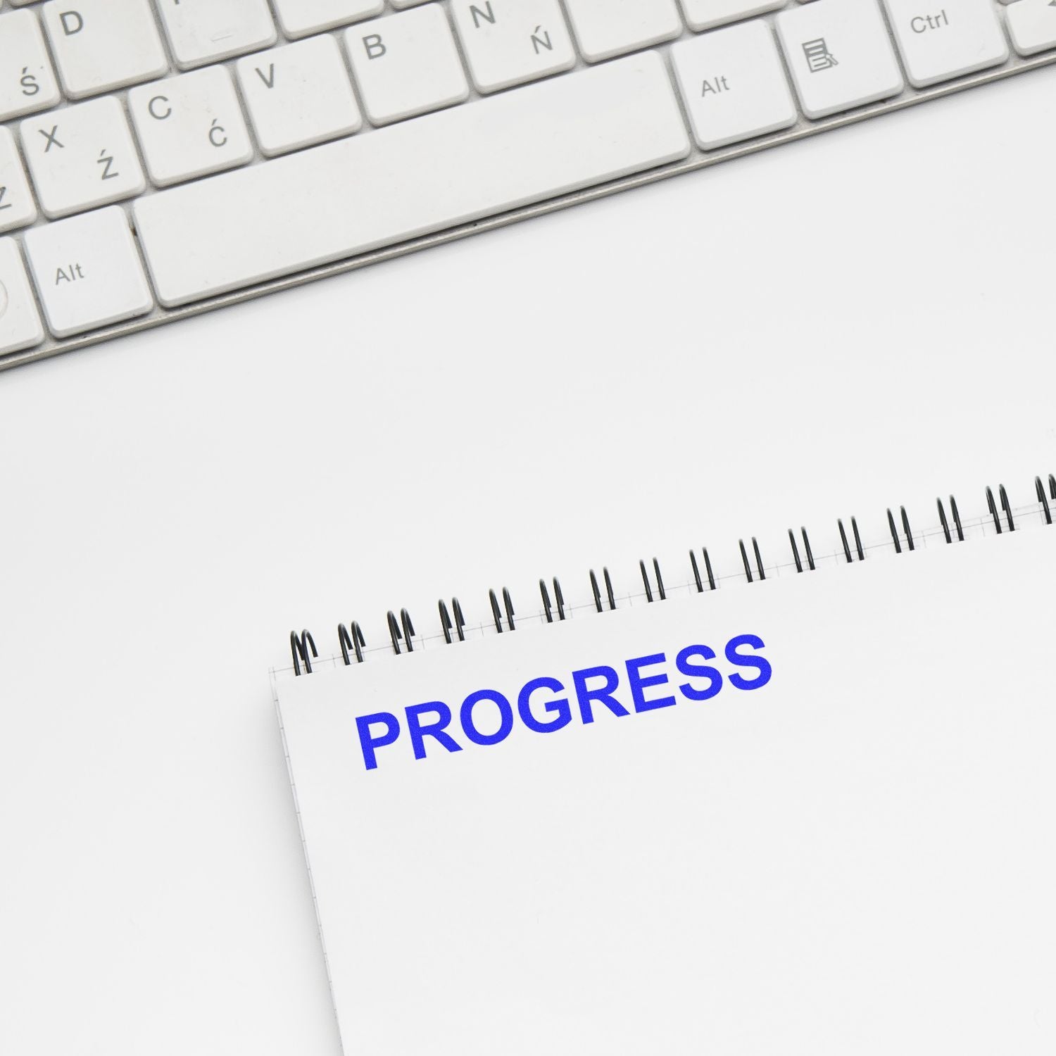 White keyboard and notebook with PROGRESS text, symbolizing productivity, goal setting, and business growth.