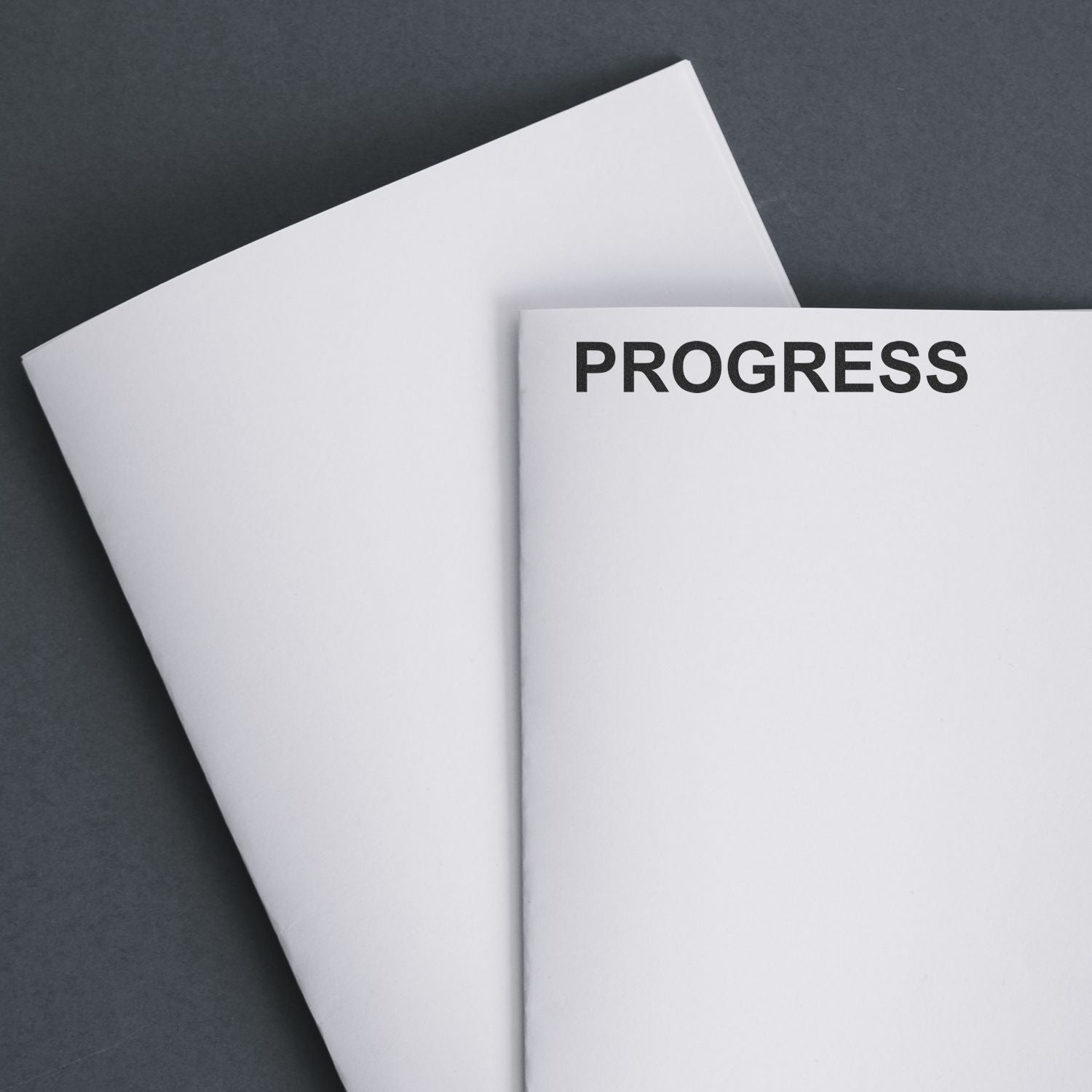 Minimalist progress concept with blank white paper sheets on a dark background and the word PROGRESS printed in bold text.