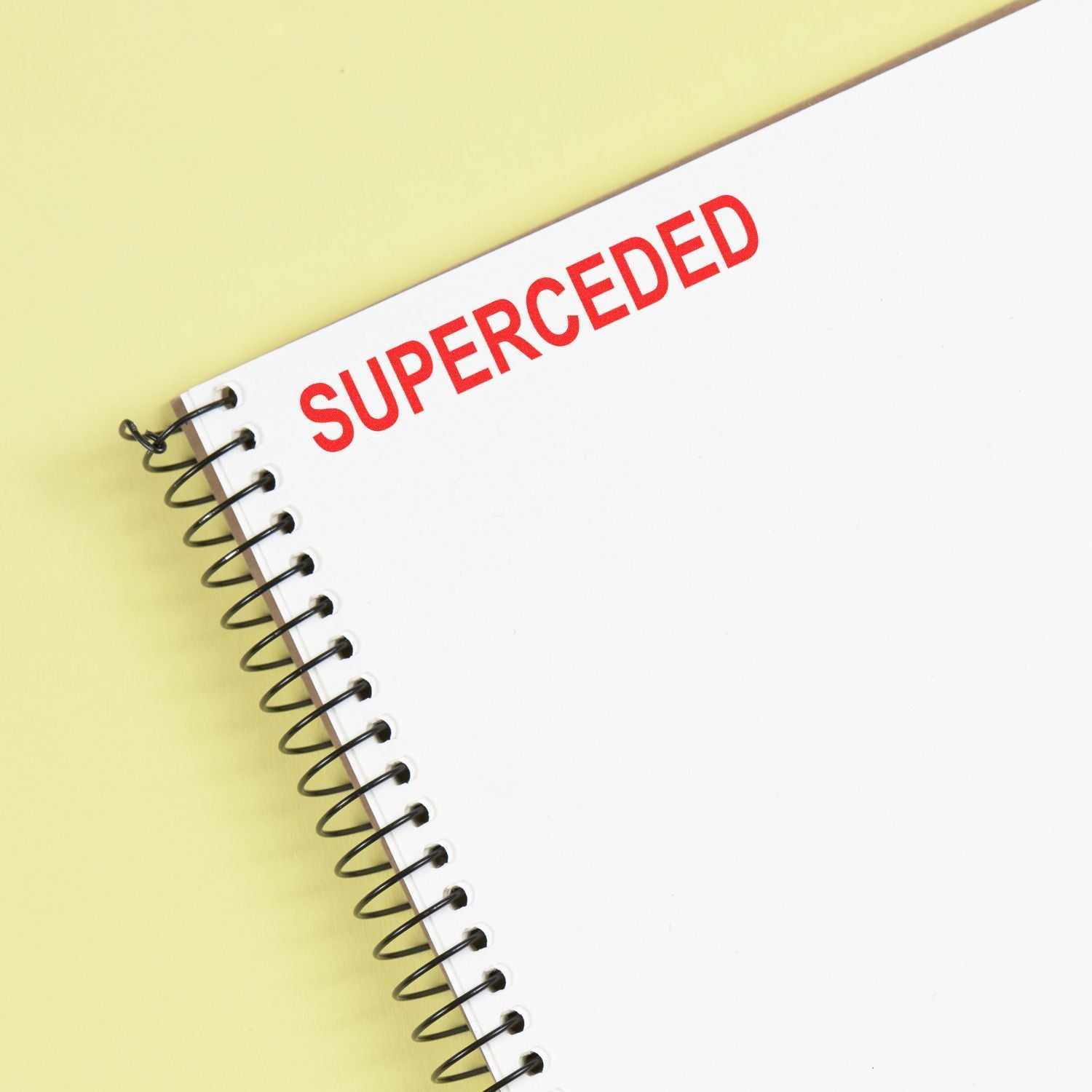 White spiral notebook with red SUPERCEDED text on a yellow background.