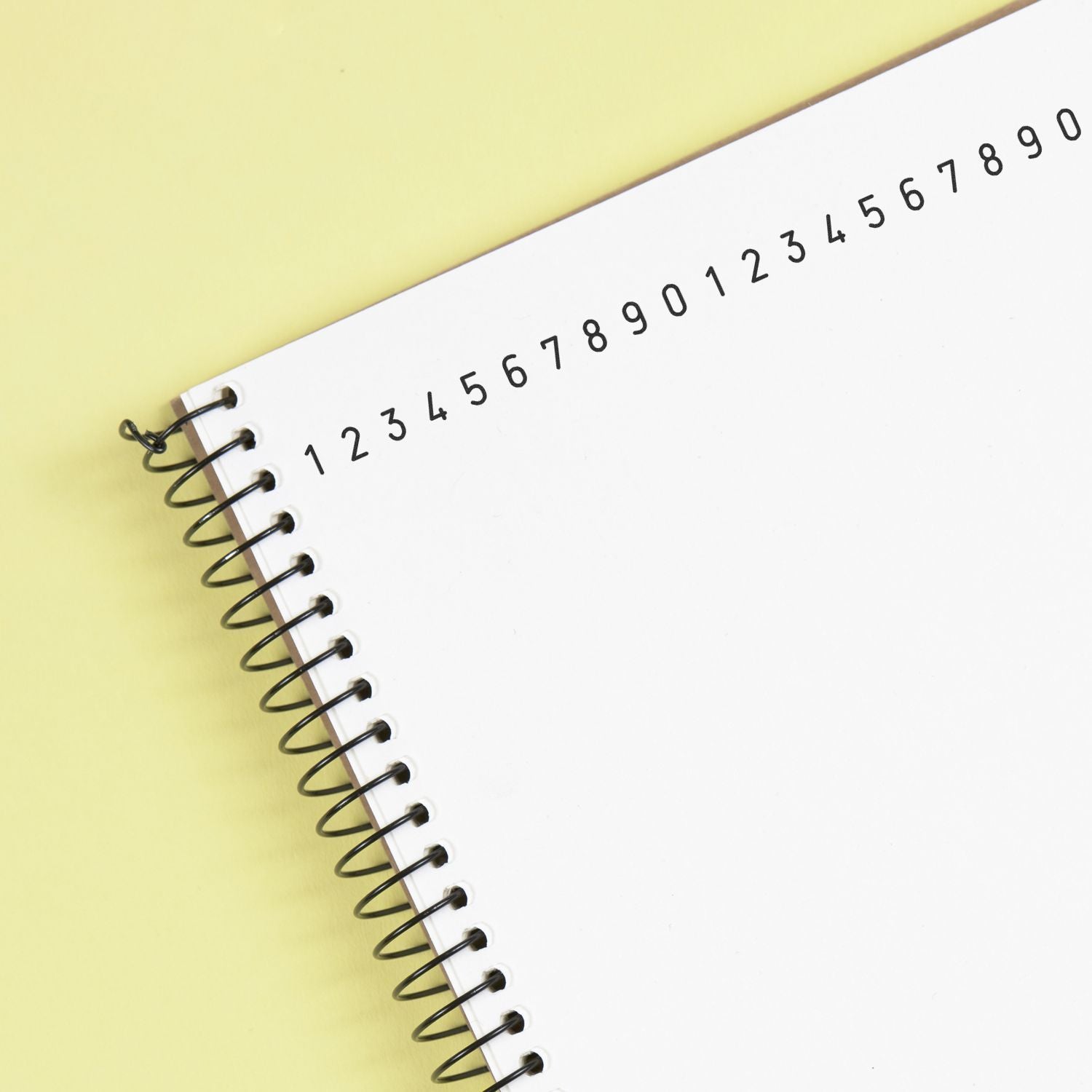 Close-up of a spiral notebook with blank numbered pages on a yellow background.