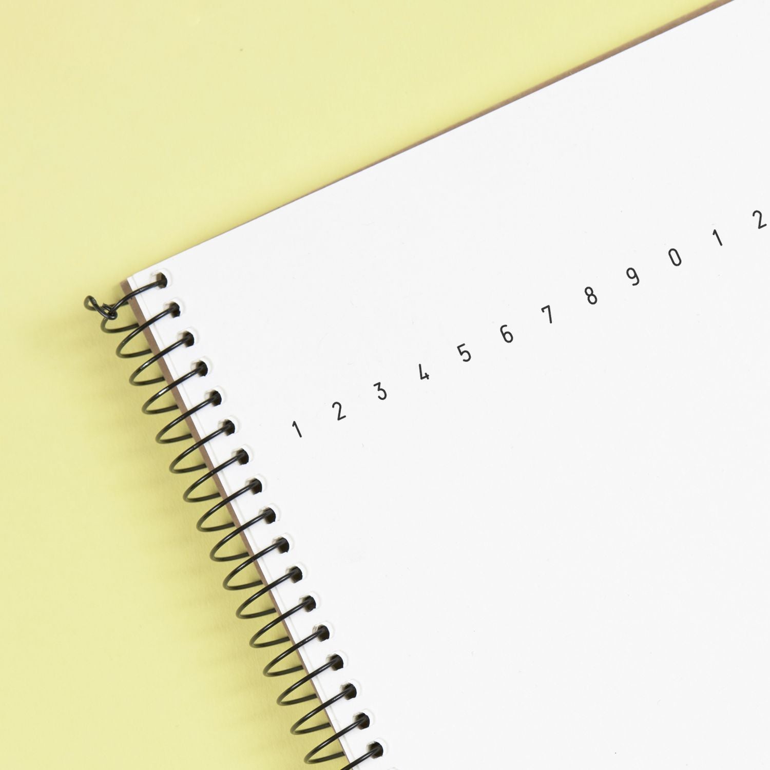 Spiral-bound notebook with numbered pages on a pastel yellow background, minimalist stationery flat lay.