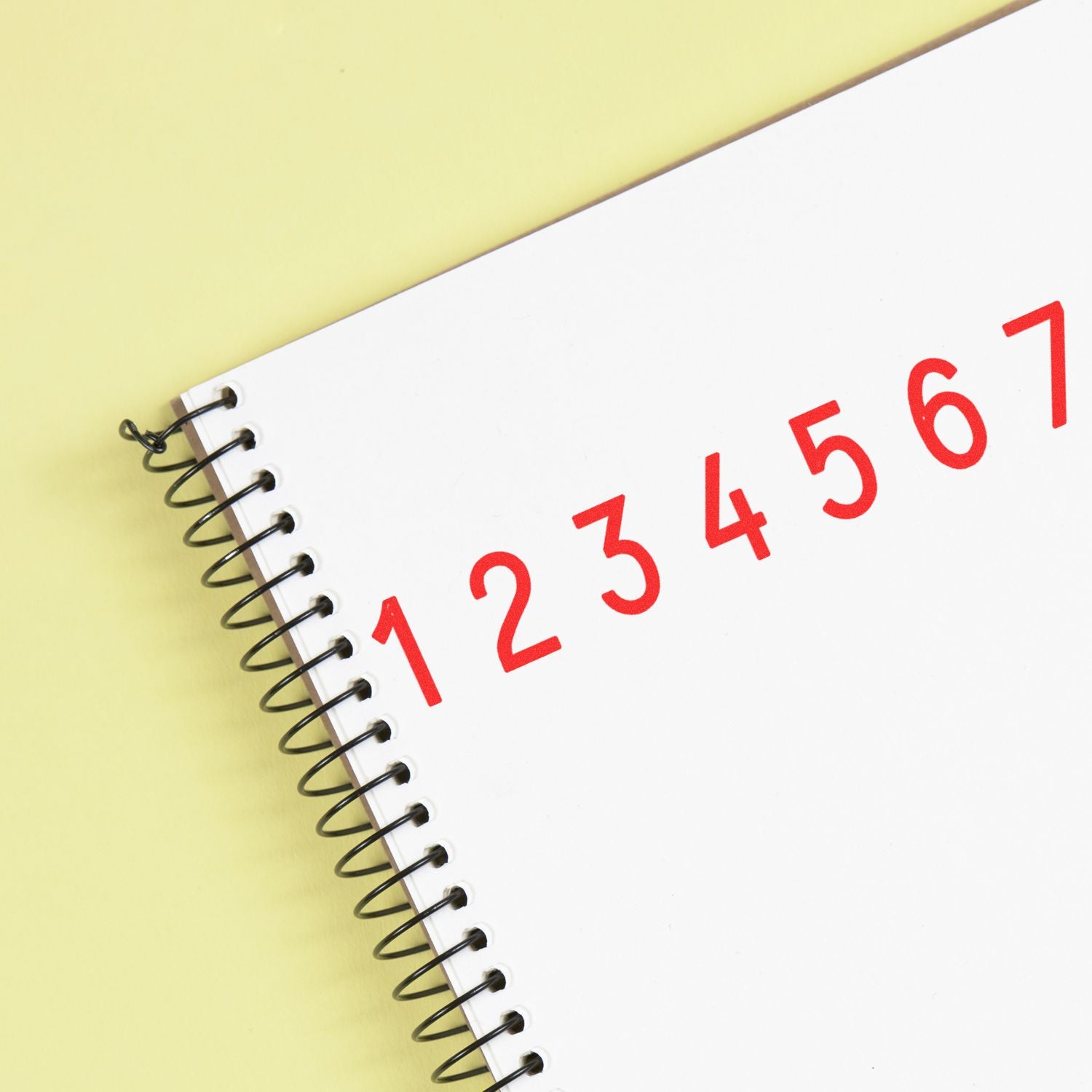 Spiral notebook with red numbers 1 through 7 on a white page against a yellow background.
