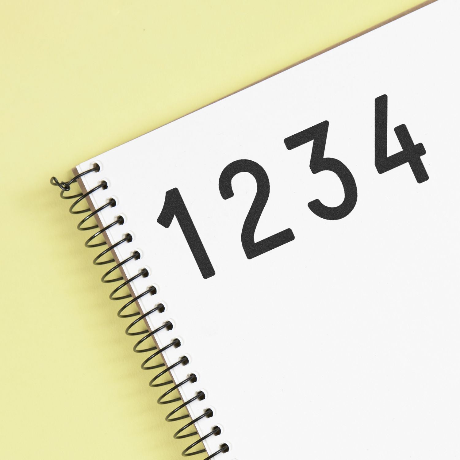 Close-up of spiral notebook with bold 1234 on a white page against a yellow background.