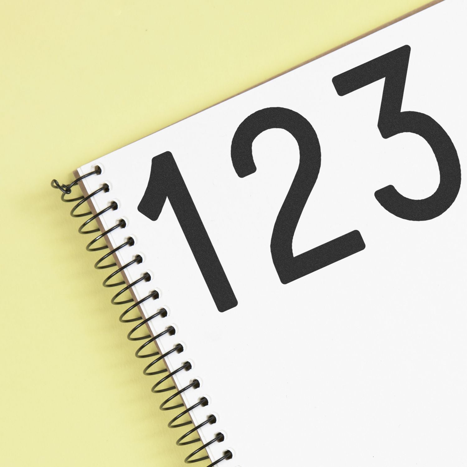Close-up of a spiral-bound calendar page with large black numbers 123 on a yellow background.