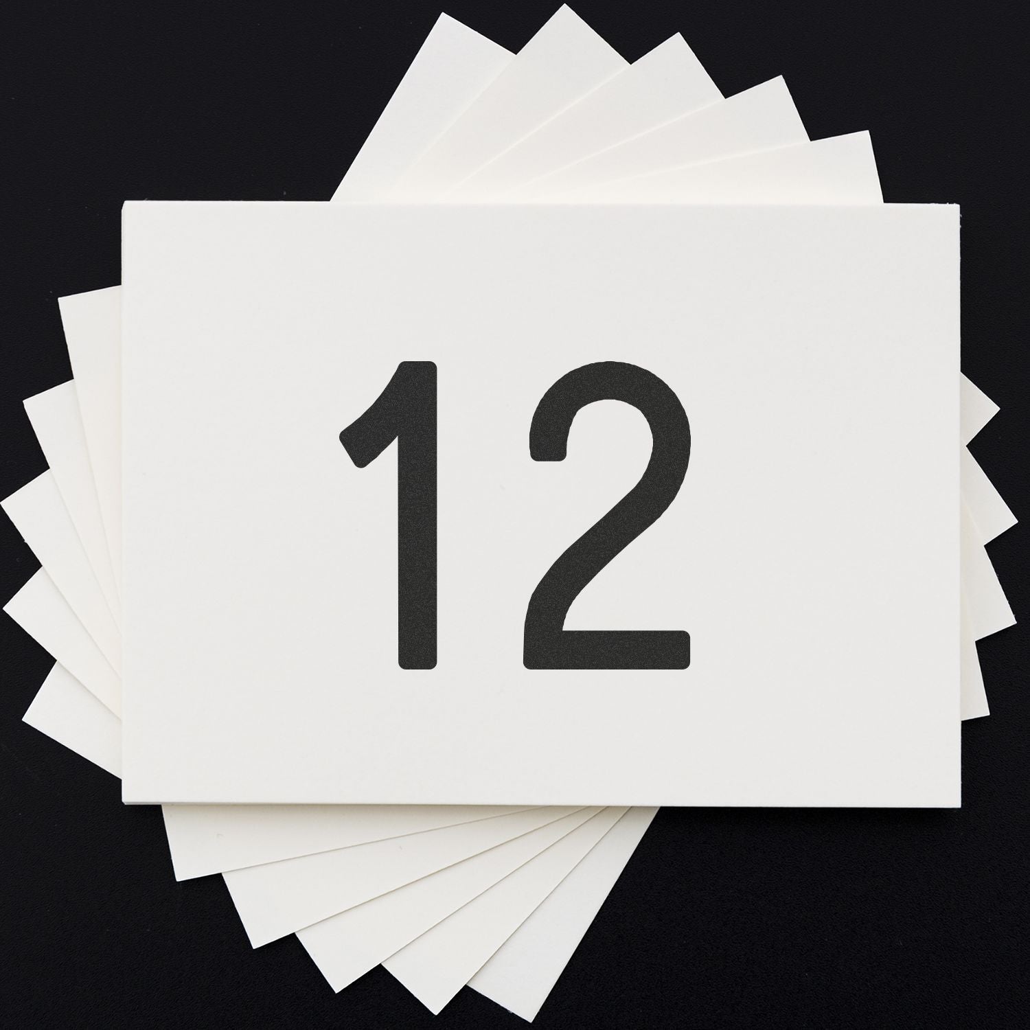 Stack of white paper cards with the number 12 on a black background, minimal calendar or countdown concept.