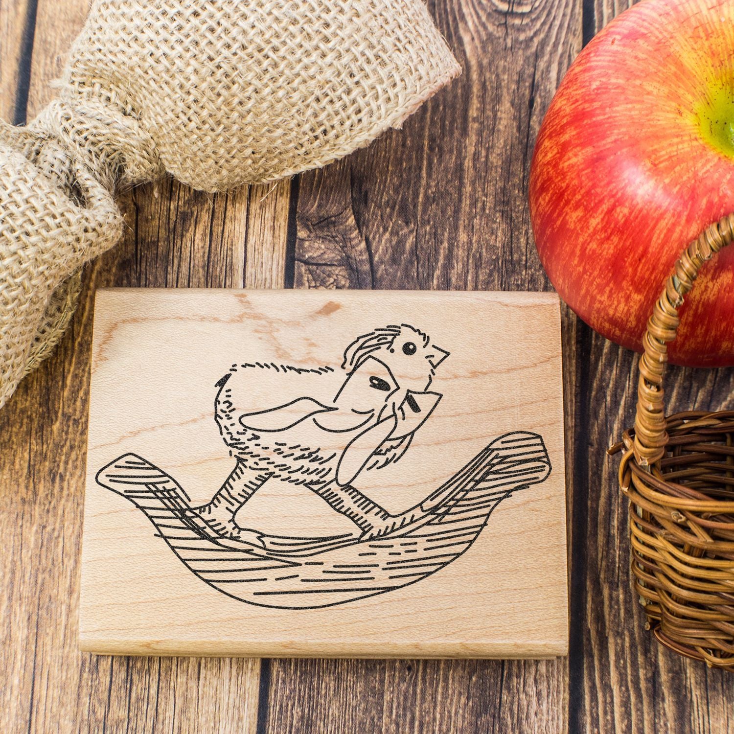Rustic wooden stamp with engraved chicken illustration on farmhouse table with burlap, apple, and wicker basket