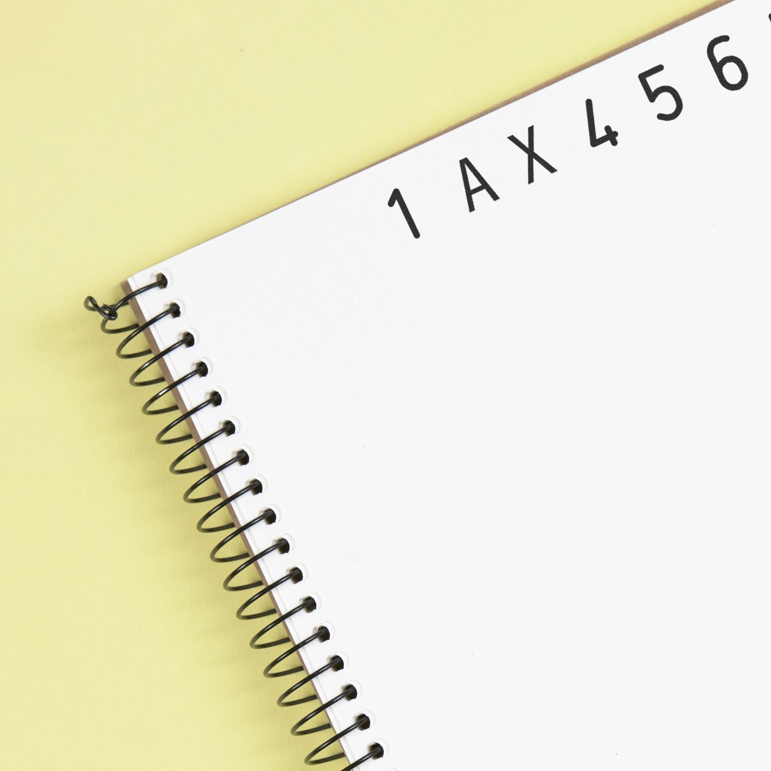 Close-up of a blank spiral notebook with black wire binding on a pastel yellow background.