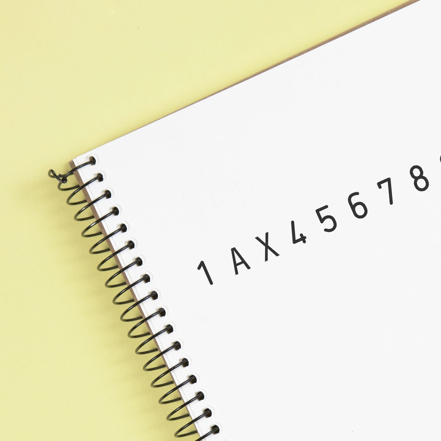 Spiral-bound notebook with alphanumeric code 1AX45678 on white cover against a yellow background.