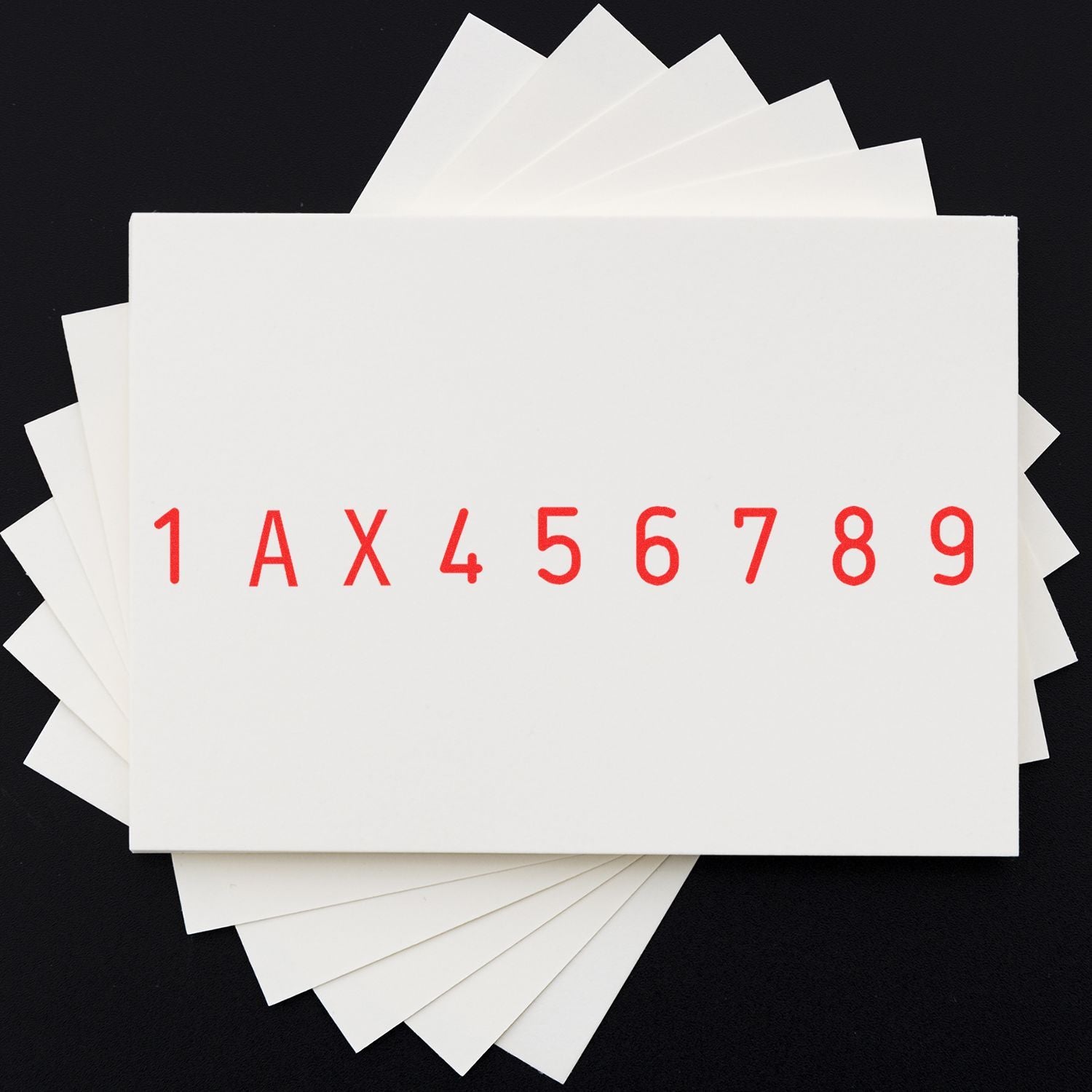 Stack of white paper sample cards with red alphanumeric code 1AX456789 on a black background