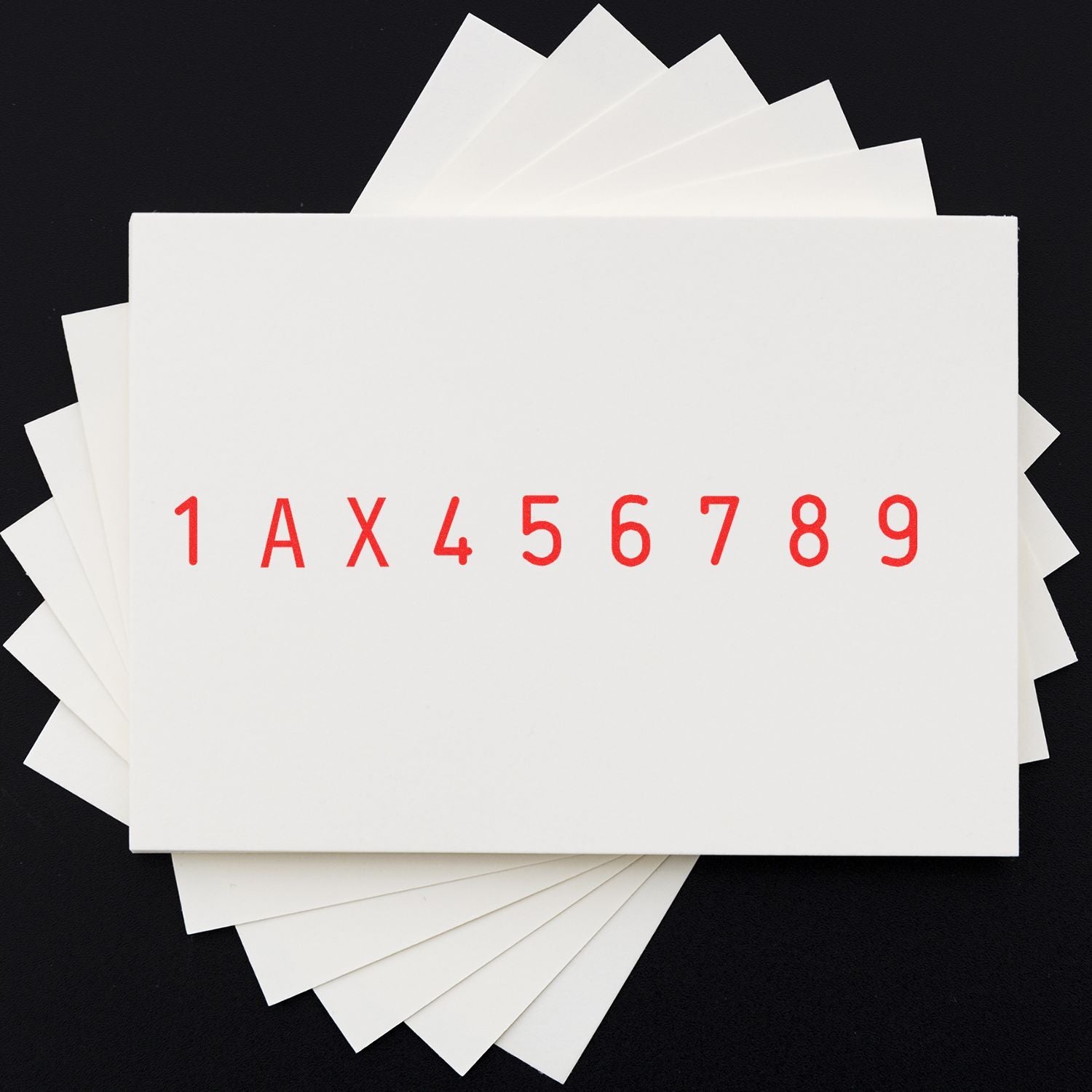 Stack of white paper swatch samples with red code 1AX456789 on black background.
