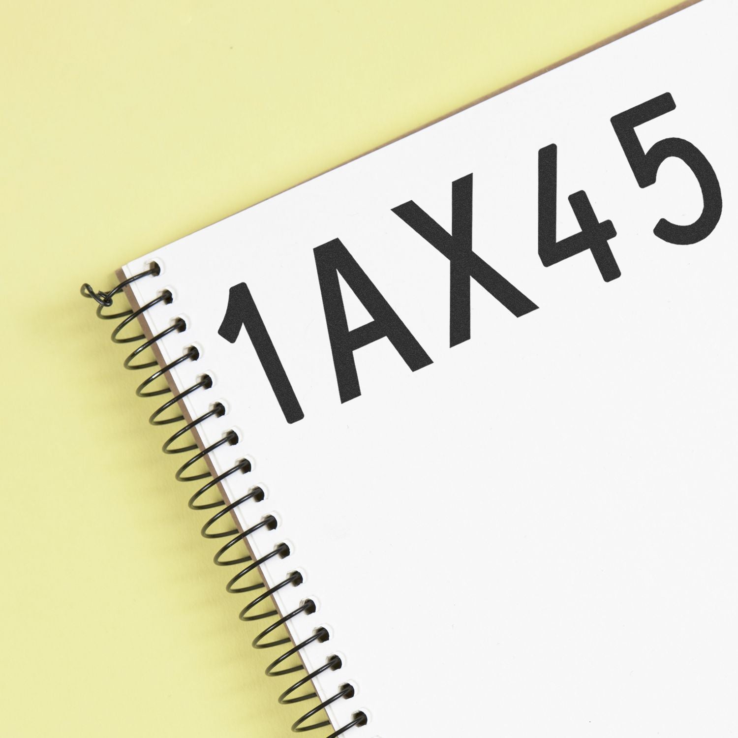 Spiral notebook with bold 1AX45 text on a white cover against a yellow background.