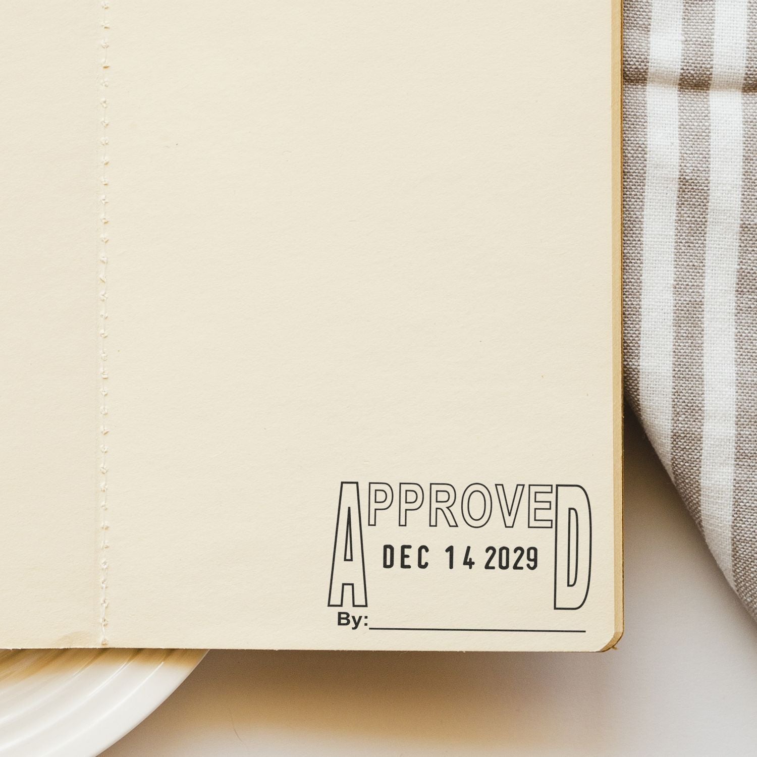 Close-up of cream notebook page with approved stamp, date Dec 14 2029, and plaid fabric background.