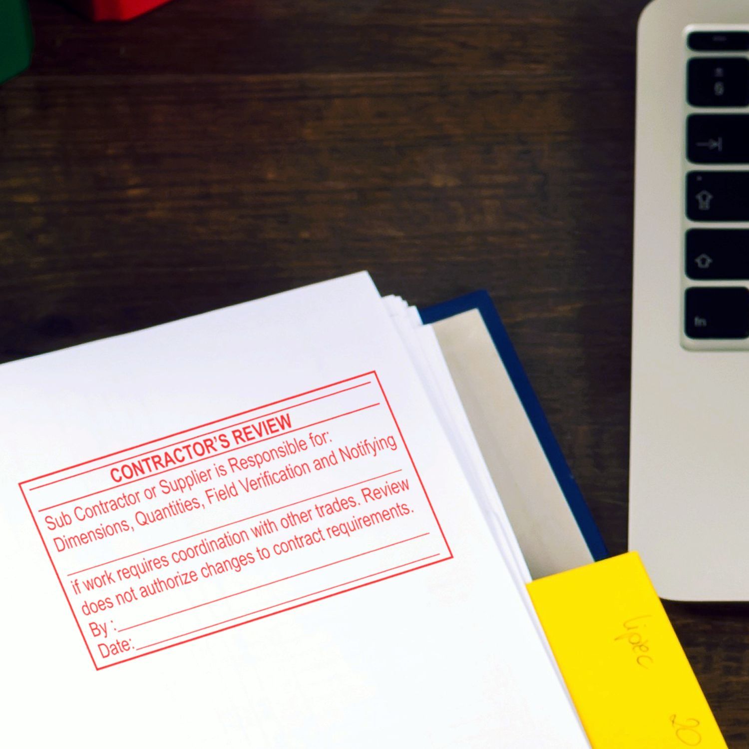 Contractors review stamped paperwork on desk next to laptop, construction document approval and project management files.