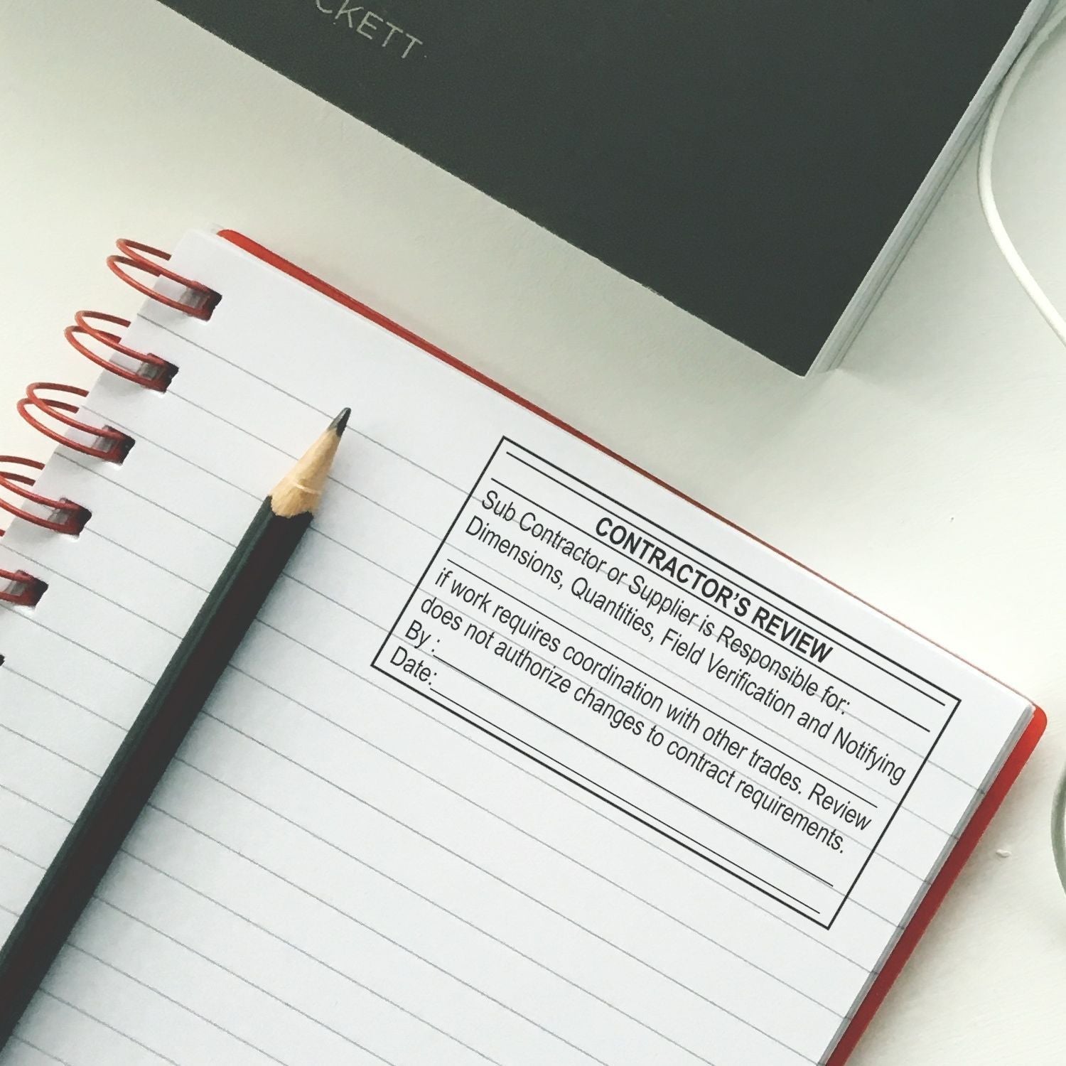 Notebook with pencil on contractor review form, construction project planning document on desk.