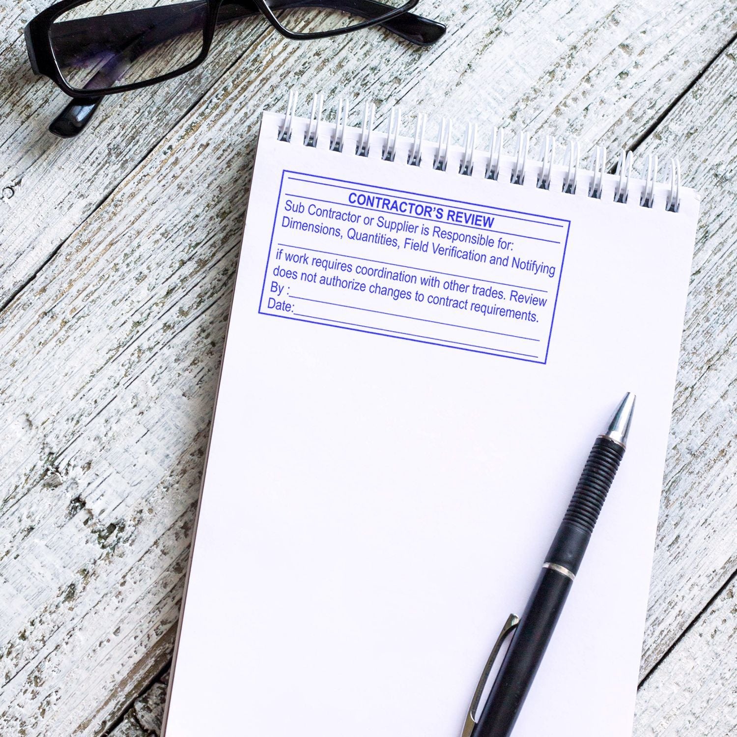 Contractors review notepad with pen and glasses on rustic wooden desk.