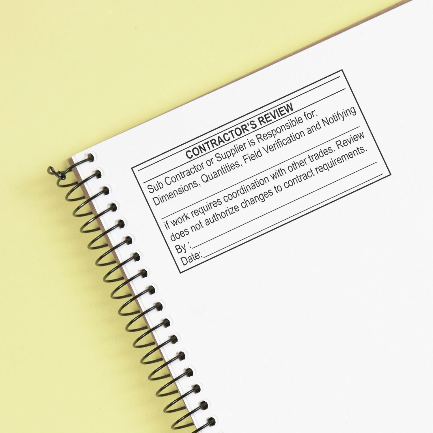 Spiral notebook with contractors review stamp on white page, concept of construction project approval and planning.