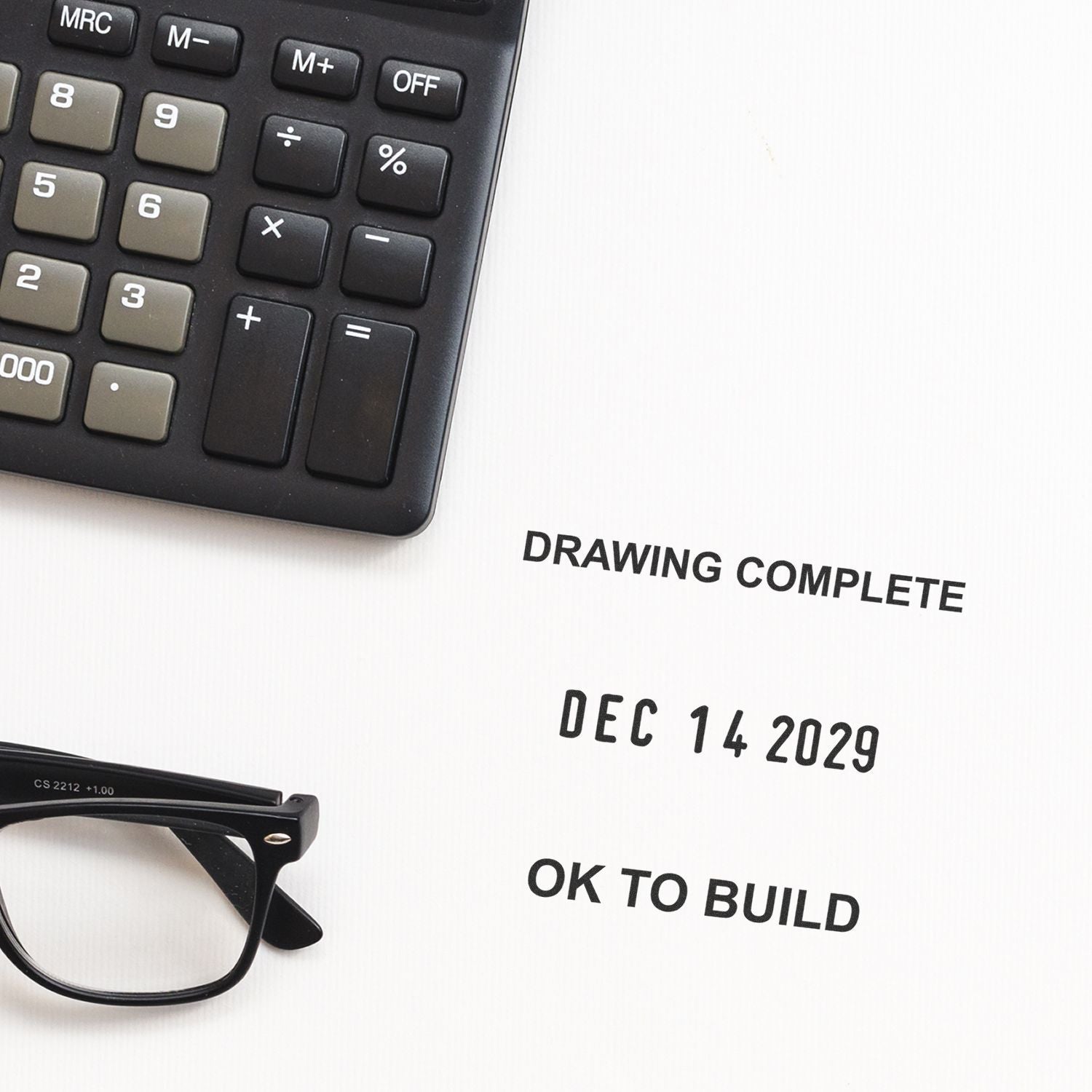 Calculator and eyeglasses on an engineering blueprint marked Drawing Complete and OK to Build with date Dec 14, 2029.