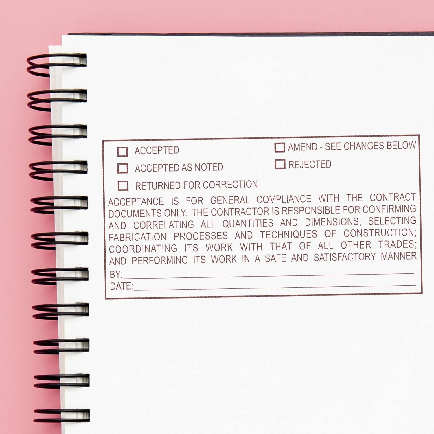 Spiral notebook page with construction approval checklist stamp on pink background