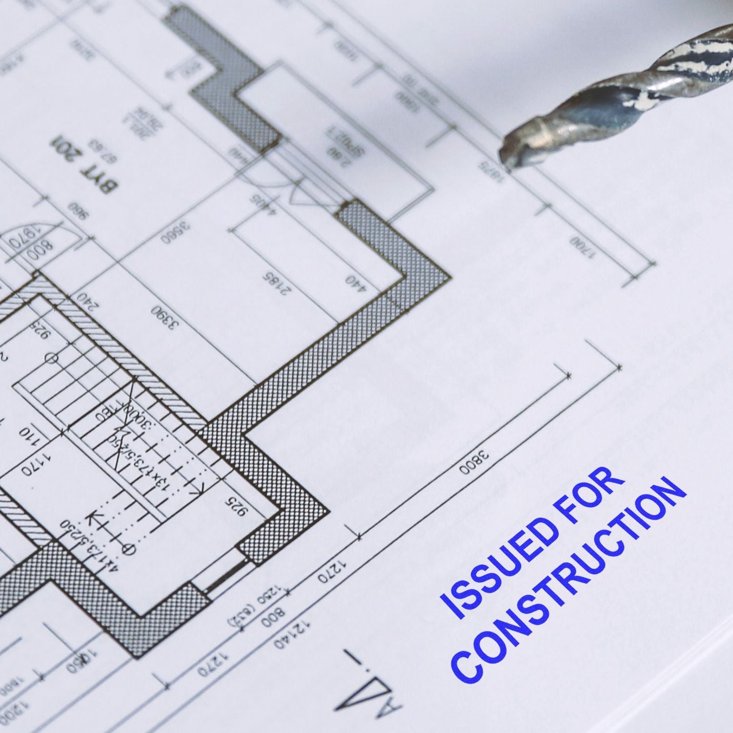 Construction blueprint with drill bit and Issued for Construction text on engineering drawing plan.
