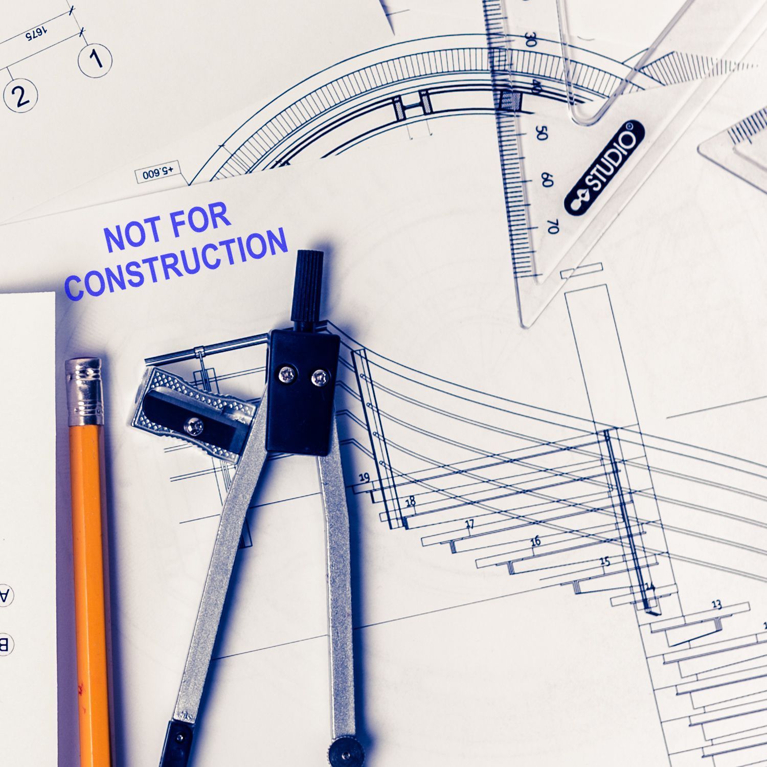Architectural blueprint with drafting compass, ruler, pencil, and Not for Construction stamp on technical drawings.