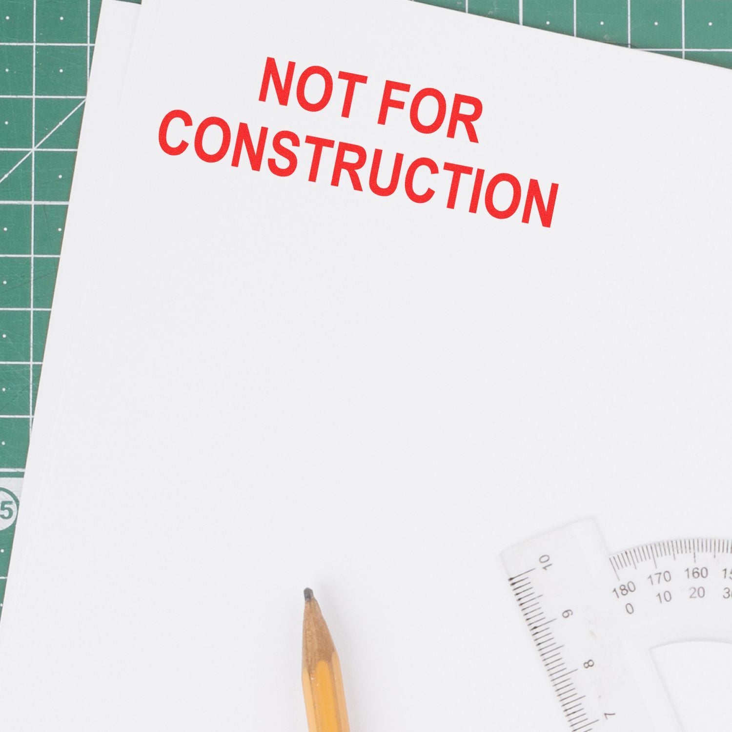 Not for construction label on paper with pencil, ruler, and protractor on green cutting mat.