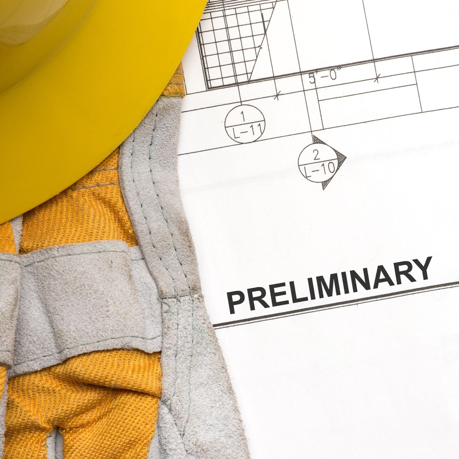 Close-up of yellow hard hat, work gloves, and preliminary construction blueprint with architectural drawing details.