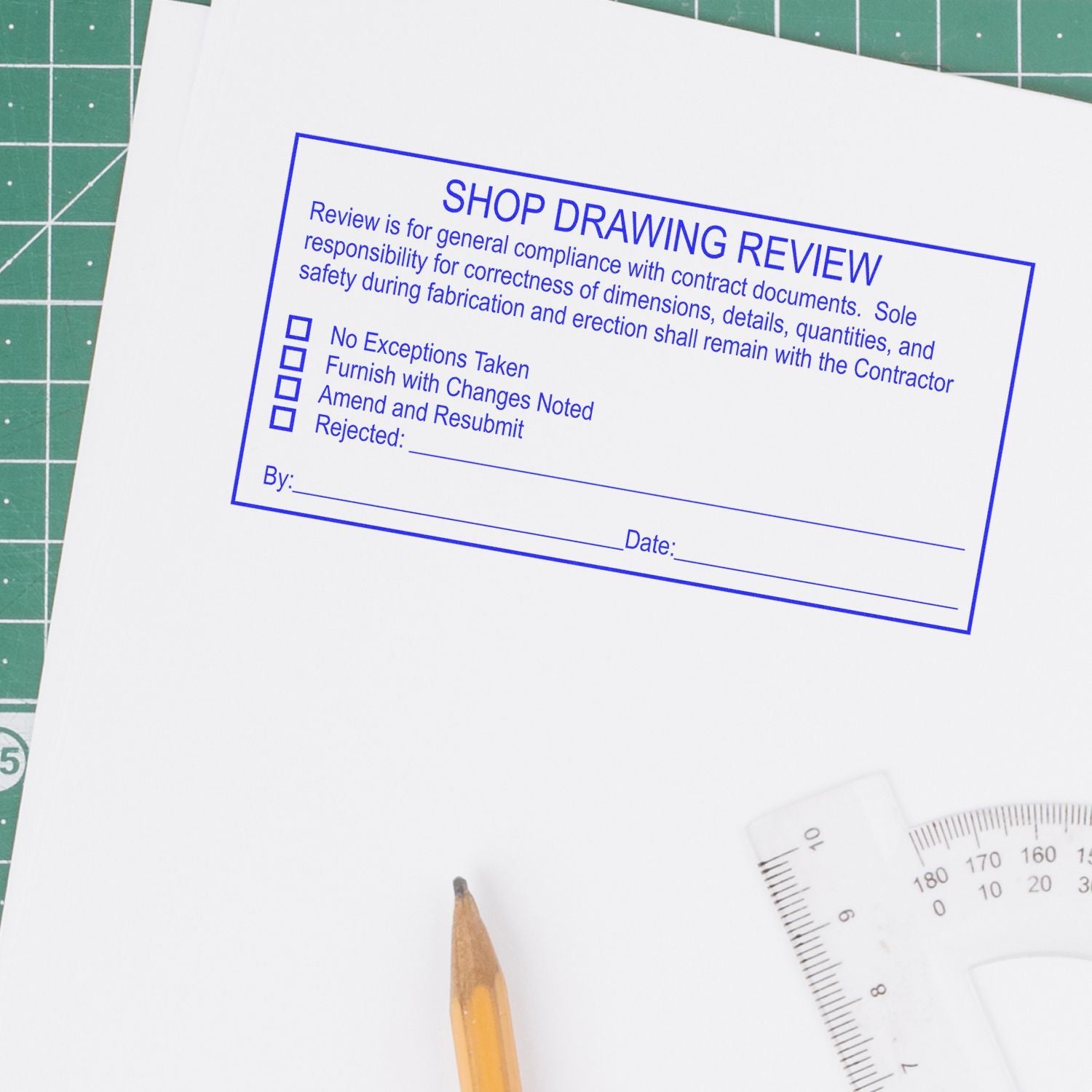Shop drawing review stamp on architectural plans with pencil and drafting tools on a cutting mat.