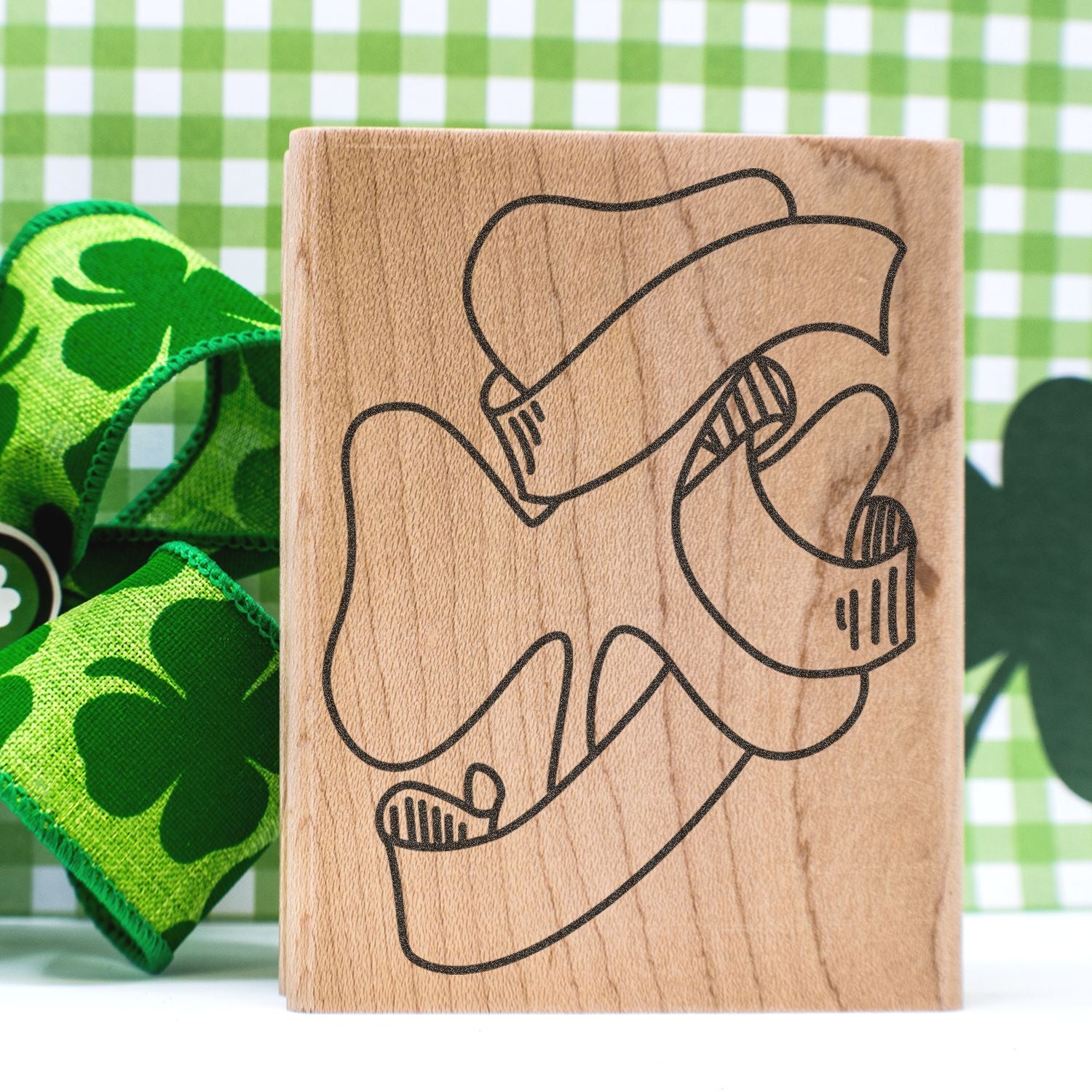 Wooden block with minimalist abstract line art face, styled with green shamrock fabric and St. Patricks Day decor background.