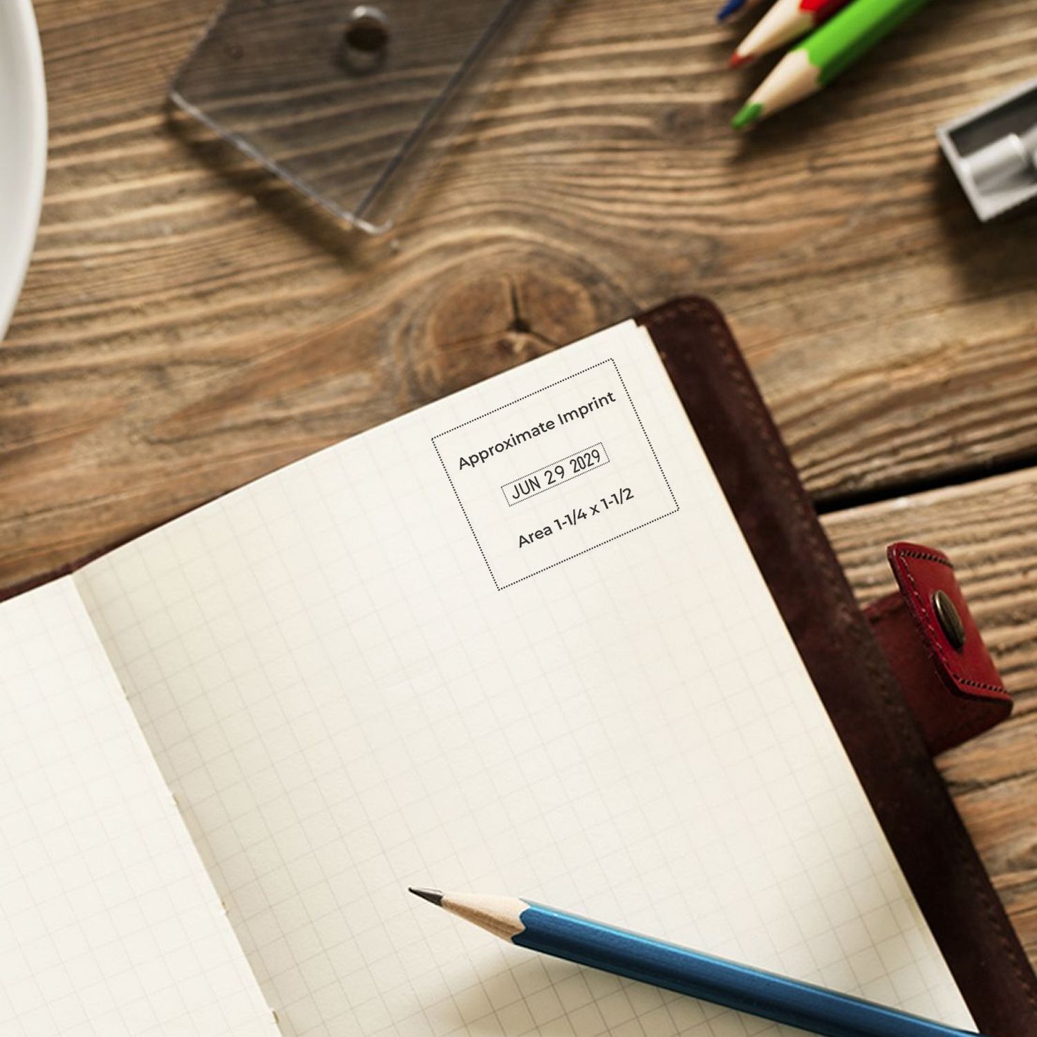Open notebook on wooden desk with pencils and approximate imprint stamp, close-up stationery workspace scene
