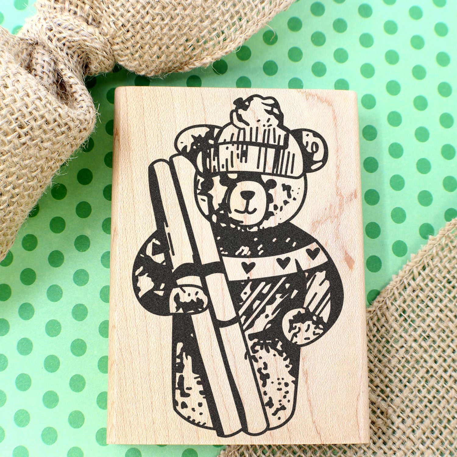 Wooden bear stamp with winter sweater and ski goggles on green polka dot background with burlap fabric.