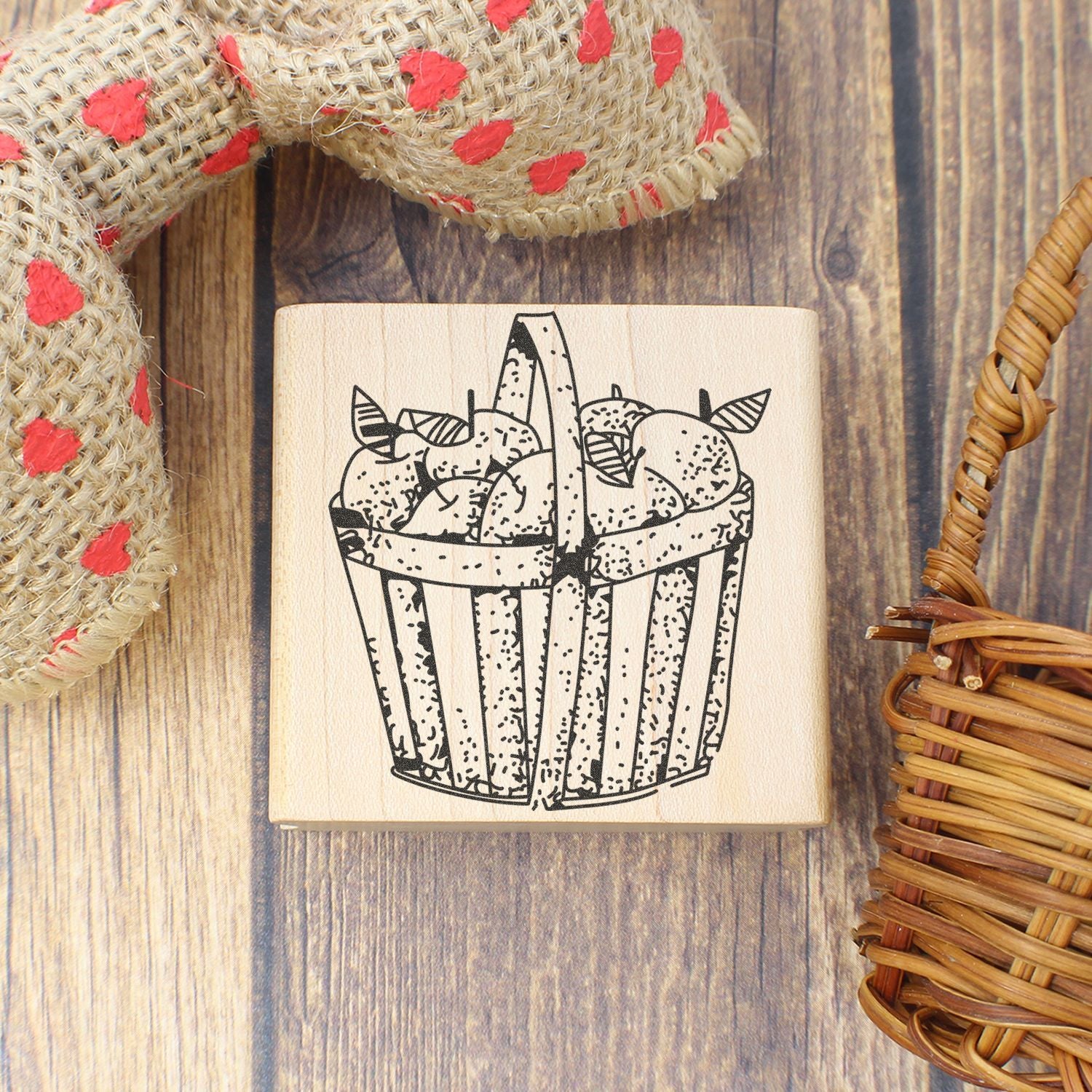 Rustic wooden stamp with hand-drawn basket of apples, styled on a wood background with burlap and wicker decor.